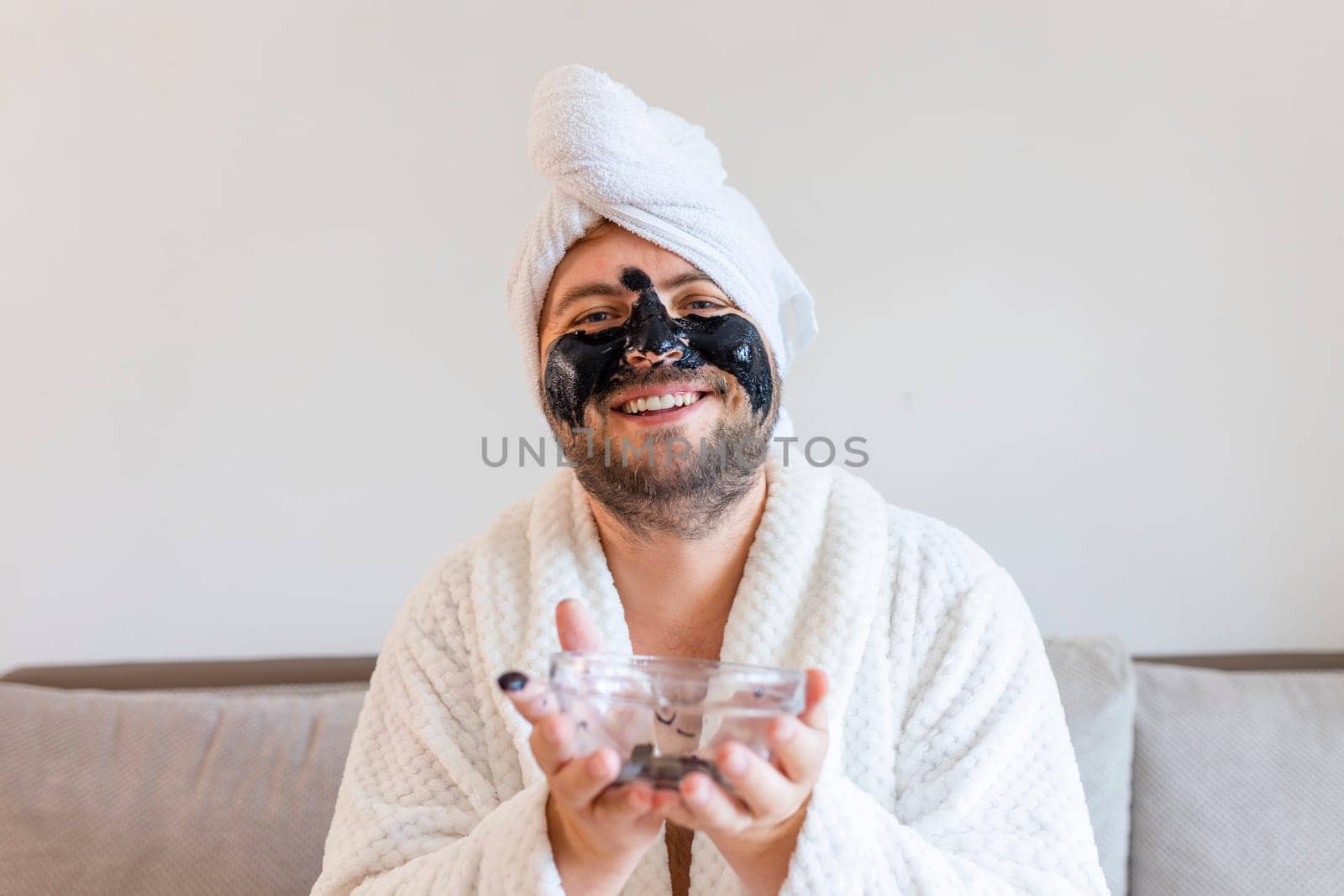 funny bearded man applying black mask for skin care