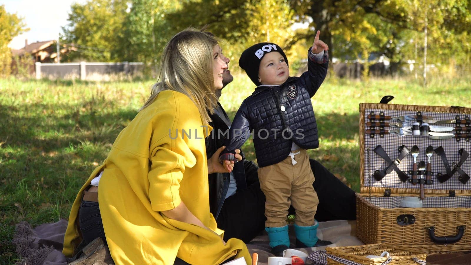 Young family with son at a picnic in the park on a sunny day. Family having picnic outdoors. Young smiling family doing a picnic on an autumns day. Family picnicking together.