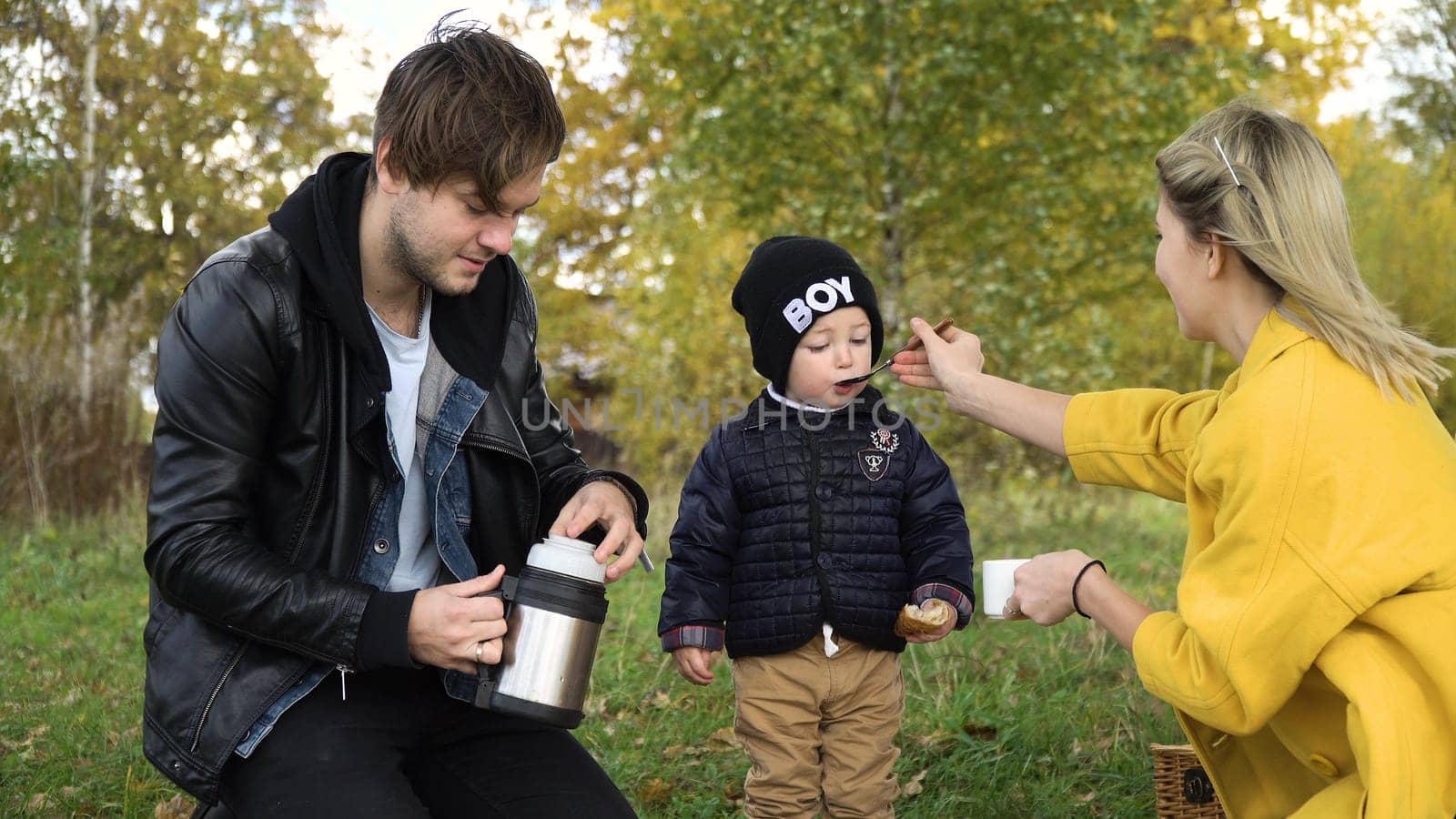 Young family with son at a picnic in the park on a sunny day. Family having picnic outdoors. Young smiling family doing a picnic on an autumns day. Family picnicking together.