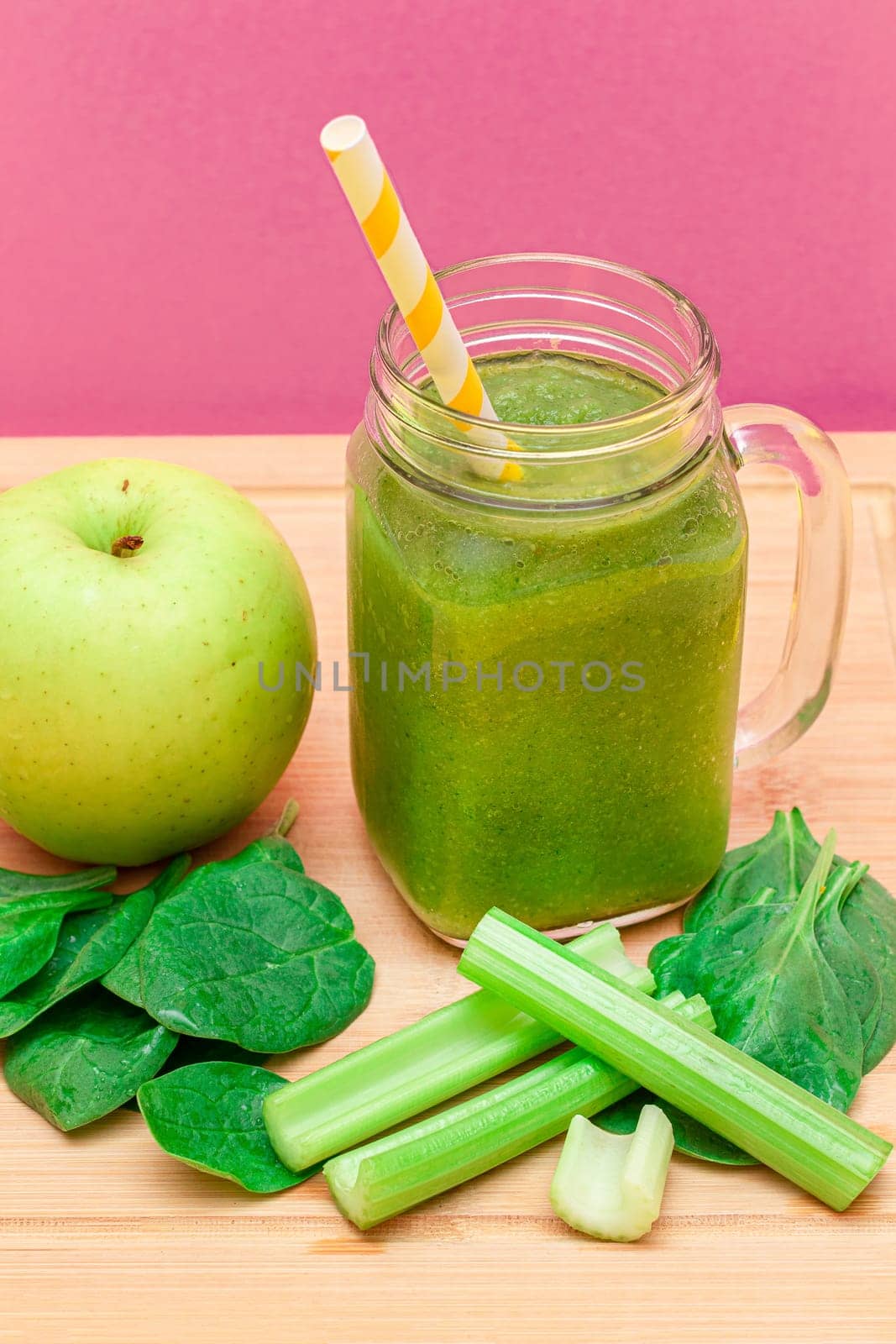 Fresh Green Smoothie of Apple, Celery, and Spinach in Glass Smoothie Jar with Yellow Cocktail Straw on Wooden Cutting Board. Vegan Detox Drink. Vegetarian Culture. Healthy Eating and Fruit Diet