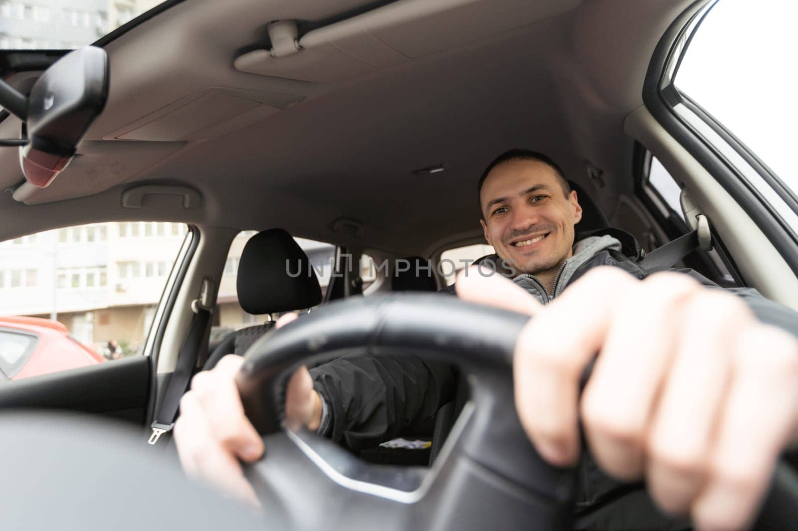 Success in motion. Handsome young man in full suit smiling while driving a car by Andelov13