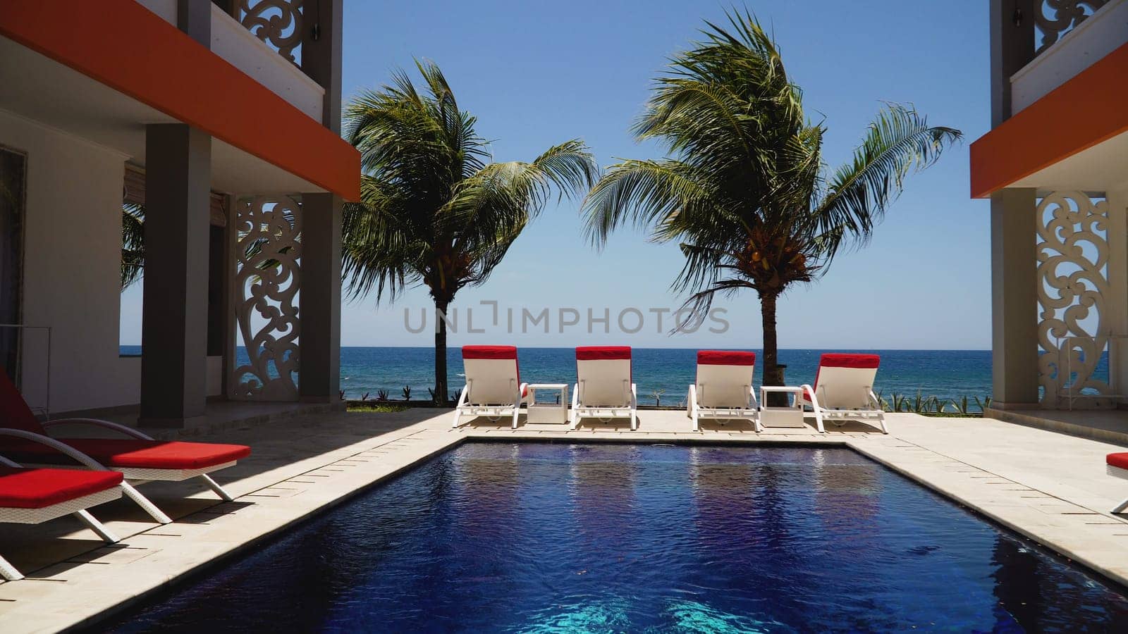 luxury hotel with swimming pool, sun beds, palm trees by sea. tropical resort with pool. Travel concept.