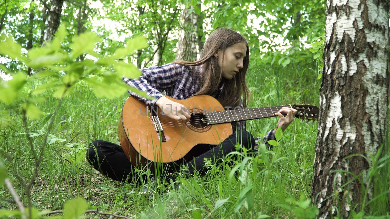 Young girl in forest with guitar in the garden. Teenage girl playing the guitar in nature. Girl play solo guitar in green nature park.