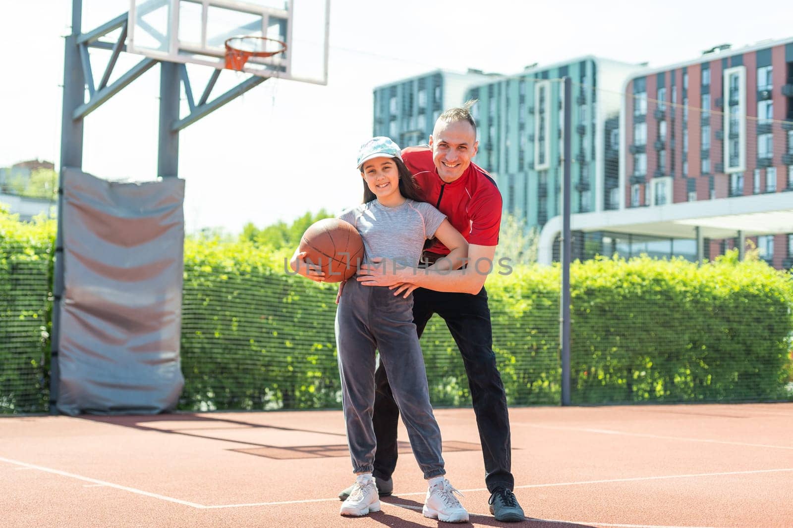 father and daughter playing basketball together on playground.