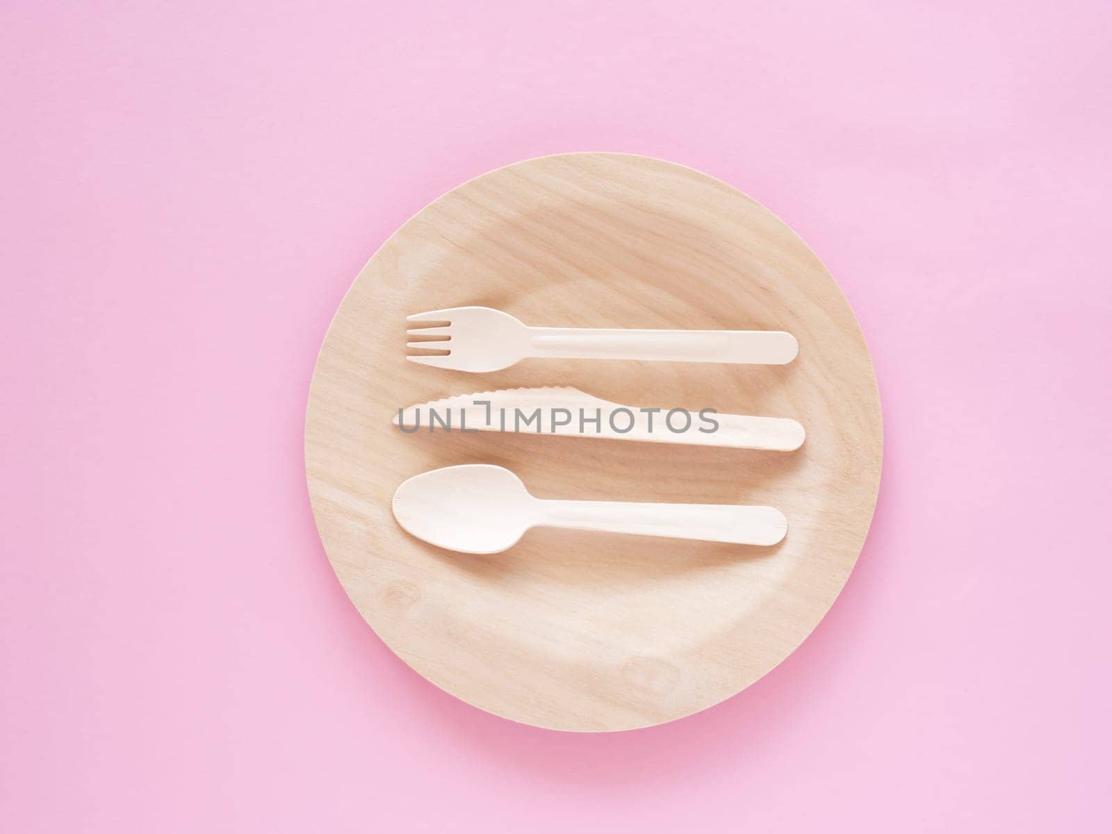 Top view of wooden, biodegradable, eco friendly tableware set on the plate on pink paper background. Concept of environment preservation and protection. Ecology, zero waste. Cope space, flat lay