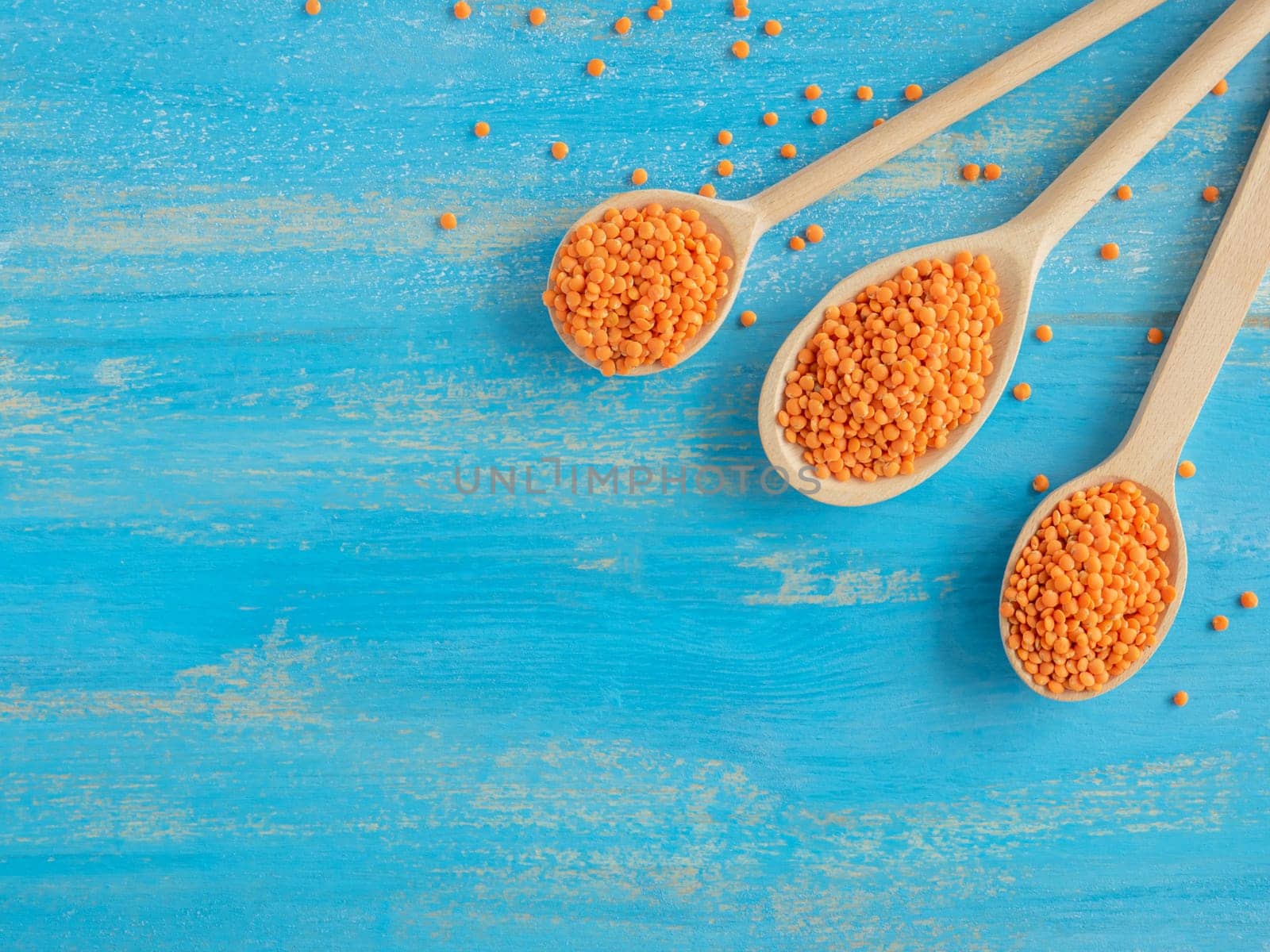 Colorful and stylish composition. Three wooden spoons with Red Lentils or Masoor Dal on light blue background. Flat lay. Vegetarian super food. Healthy eating and dietary. Canadian Orange Lentil