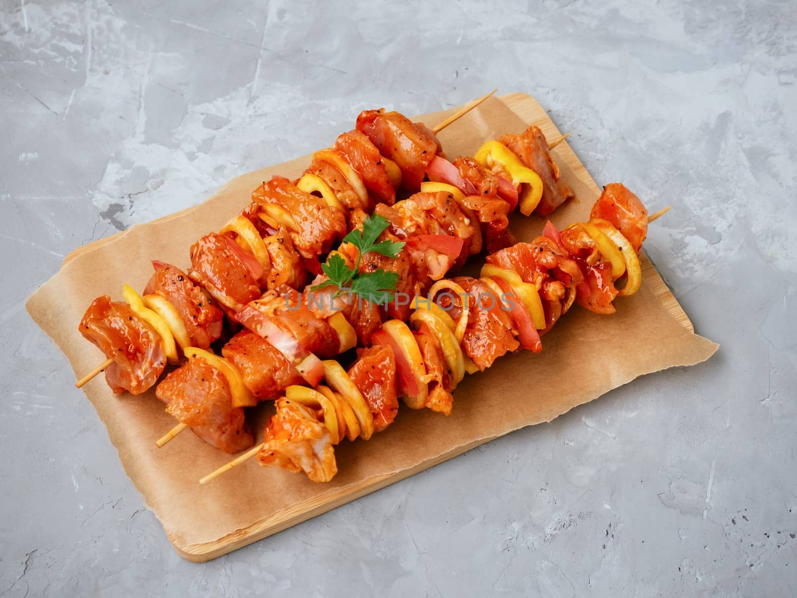Raw meat in a marinade with spices on cutting board. Uncooked marinated and rubbed chiken or turkey shish kebabs on skewers with onion, pepper and tomato ready for grilling or BBQ. Soft focus
