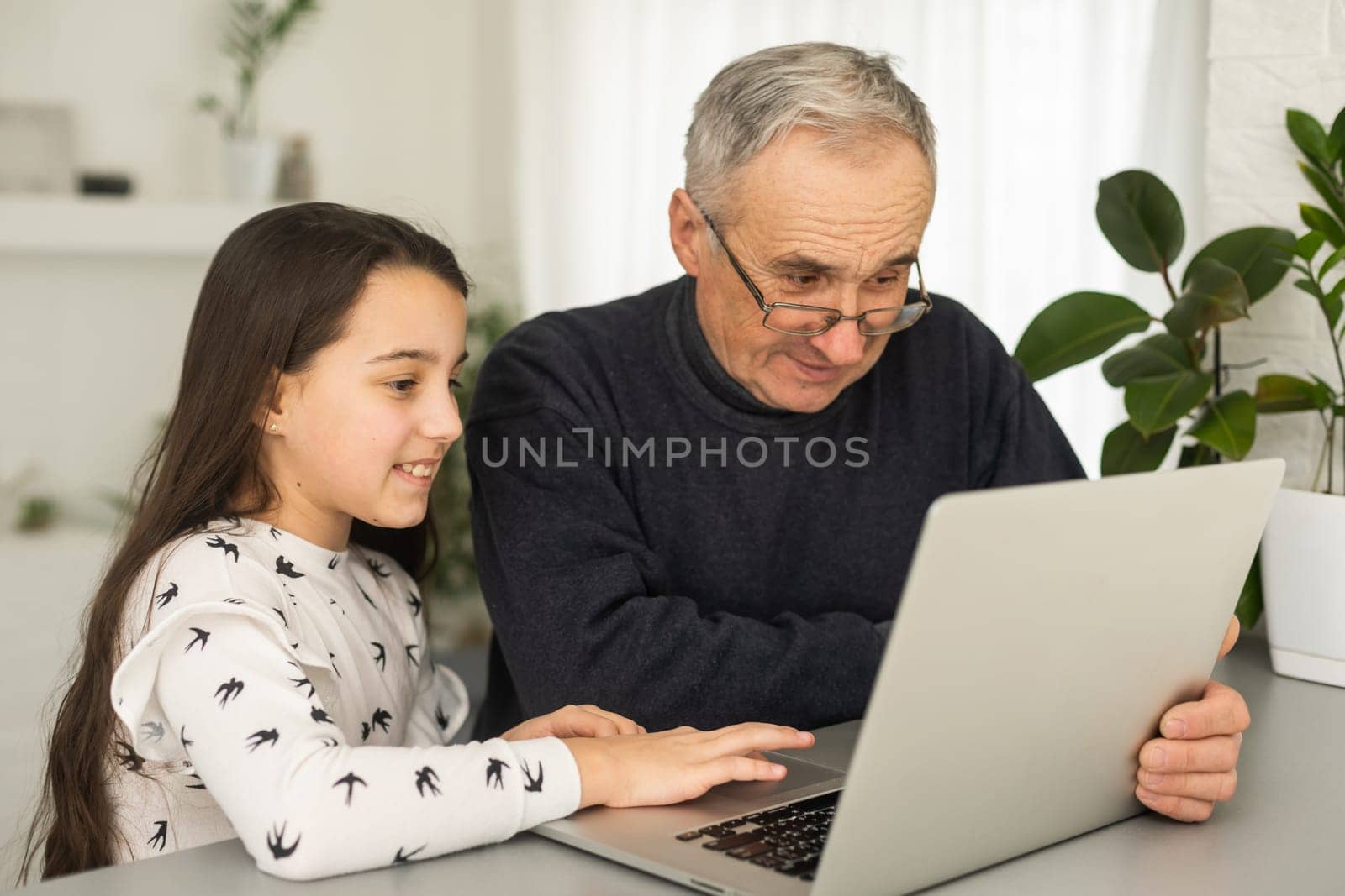 Happy retirement grandfather and pretty granddaughter laughing while watching e-book for learning to education together by laptop. Family educational at home concept. Technology and education