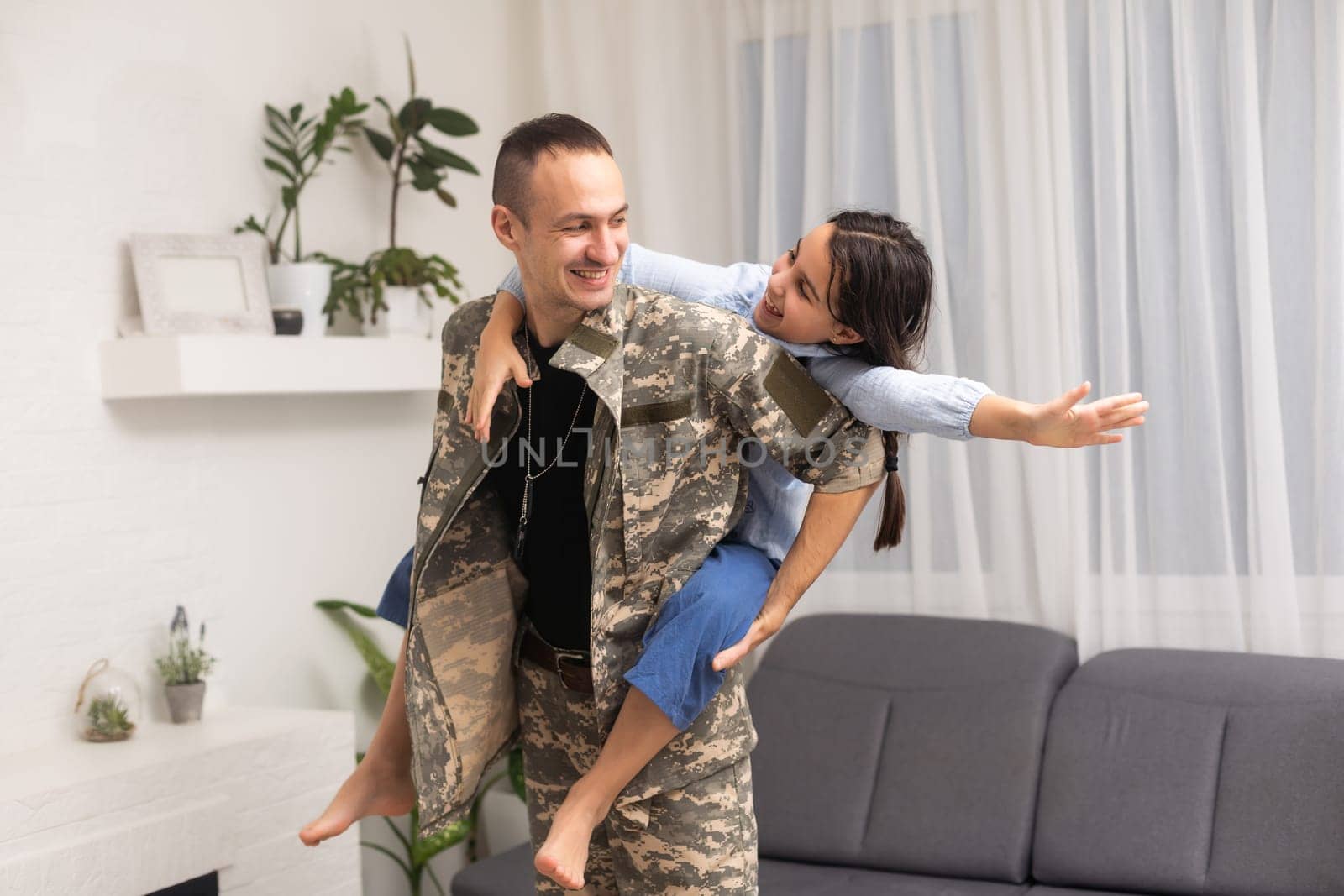 Affectionate girl looking at camera out of her father back in camouflage.