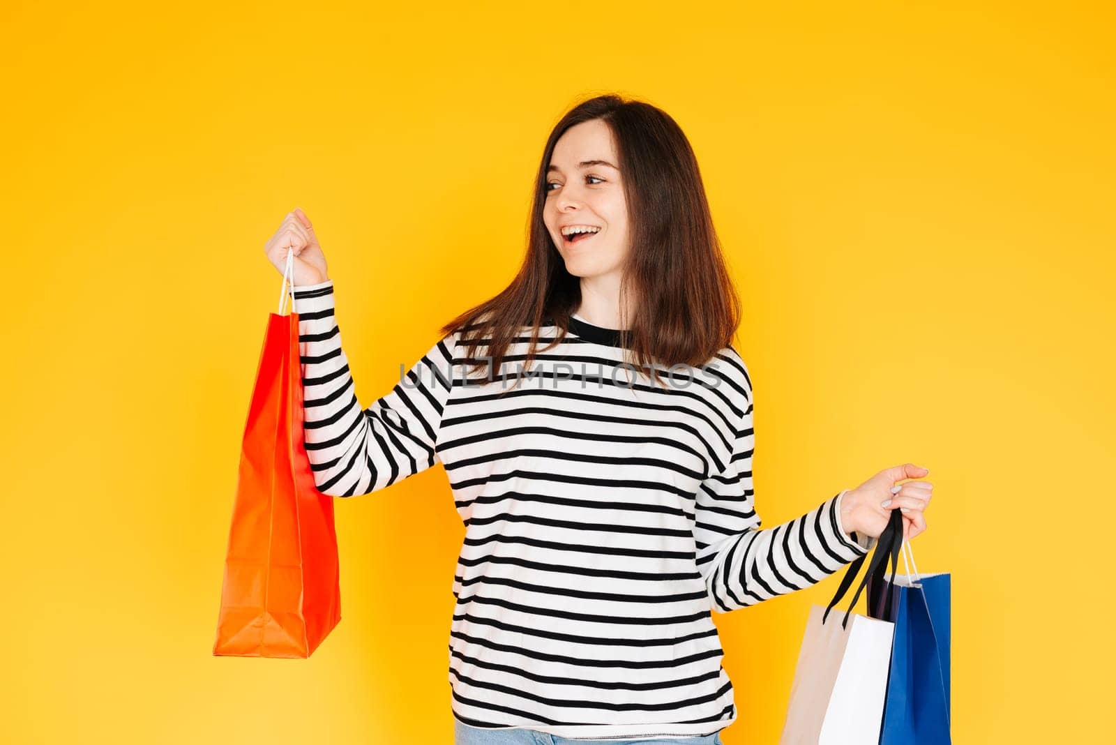 Delighted Shopper Concept: Captivating Woman Excited About Bargains and Discounts, Looking at Empty Space - Shopping Spree Mood Isolated on Vibrant Yellow Background.