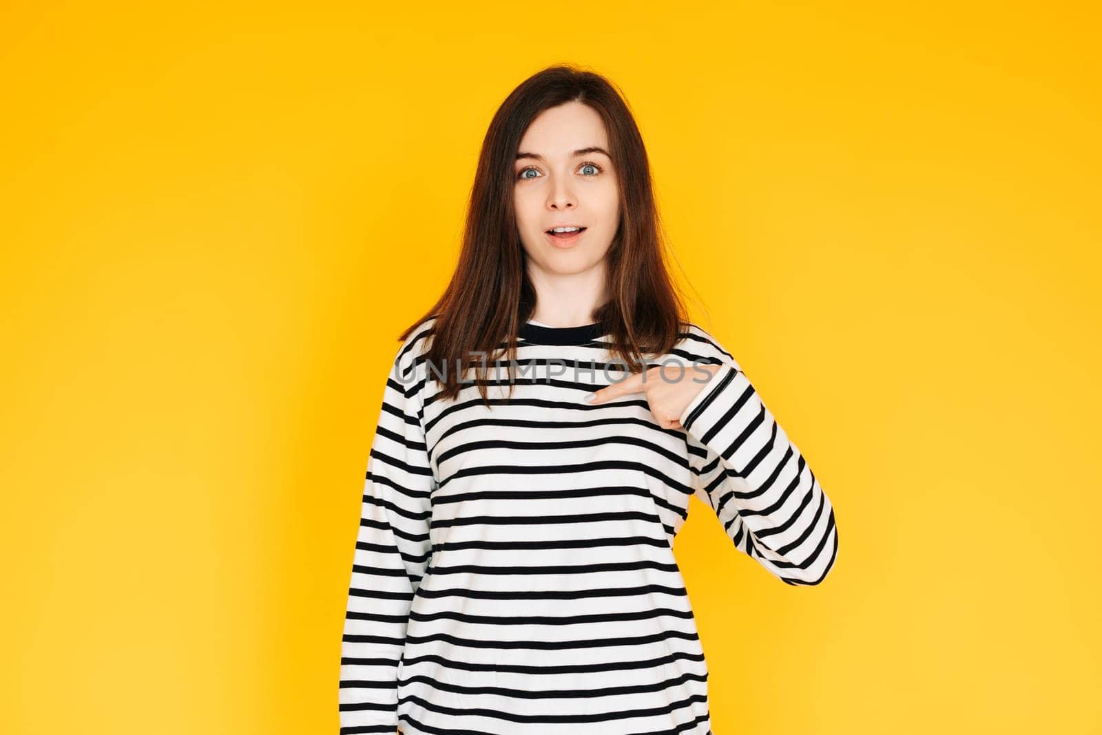 Delighted Woman Pointing at Herself in Amazement - Humorous Reaction Concept on Bright Yellow Background. Surprised and Amused Woman Pointing at Herself with Open Mouth - Self-Recognition Humor.