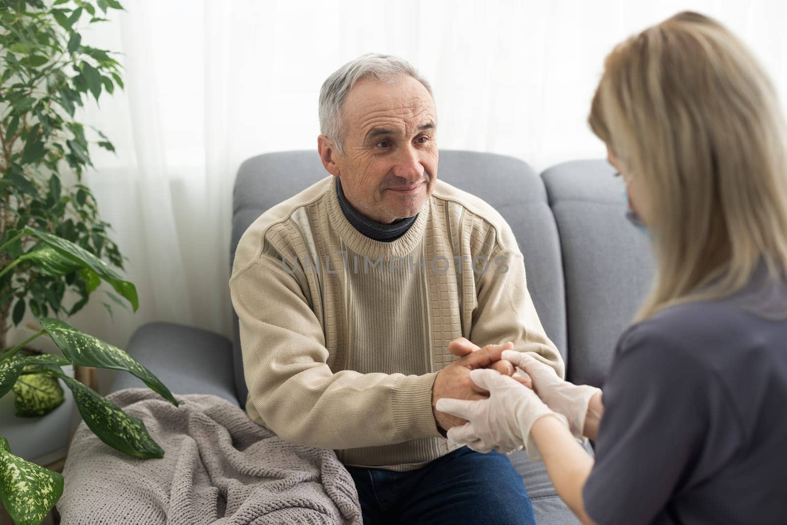 Caring nurse talks to old patient holds his hand sit in living room at homecare visit provide psychological support listen complains showing empathy encouraging. Geriatrics medicine caregiving concept.