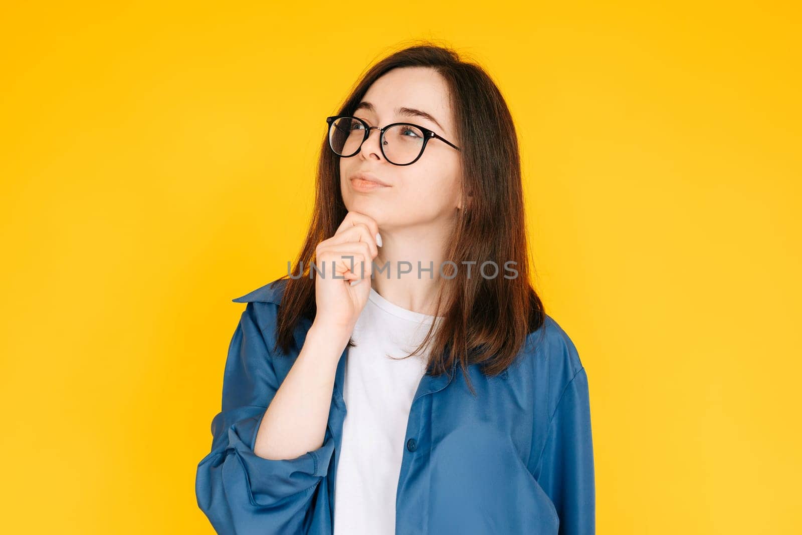Smart Shopping Decision: Stylish and Thoughtful Woman Considering New Product Purchase, Arm on Face Pose - Fashionable Consumer Concept Isolated on Yellow Background.