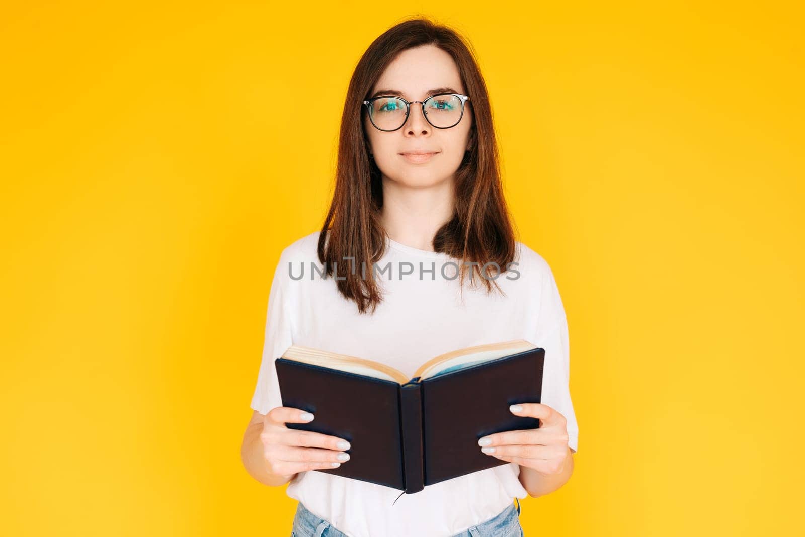 Joyful Student immersed in Reading: Cheerful Woman with Glasses Enjoying a Novel Book - Education and Leisure Concept Isolated on Vibrant Yellow Background