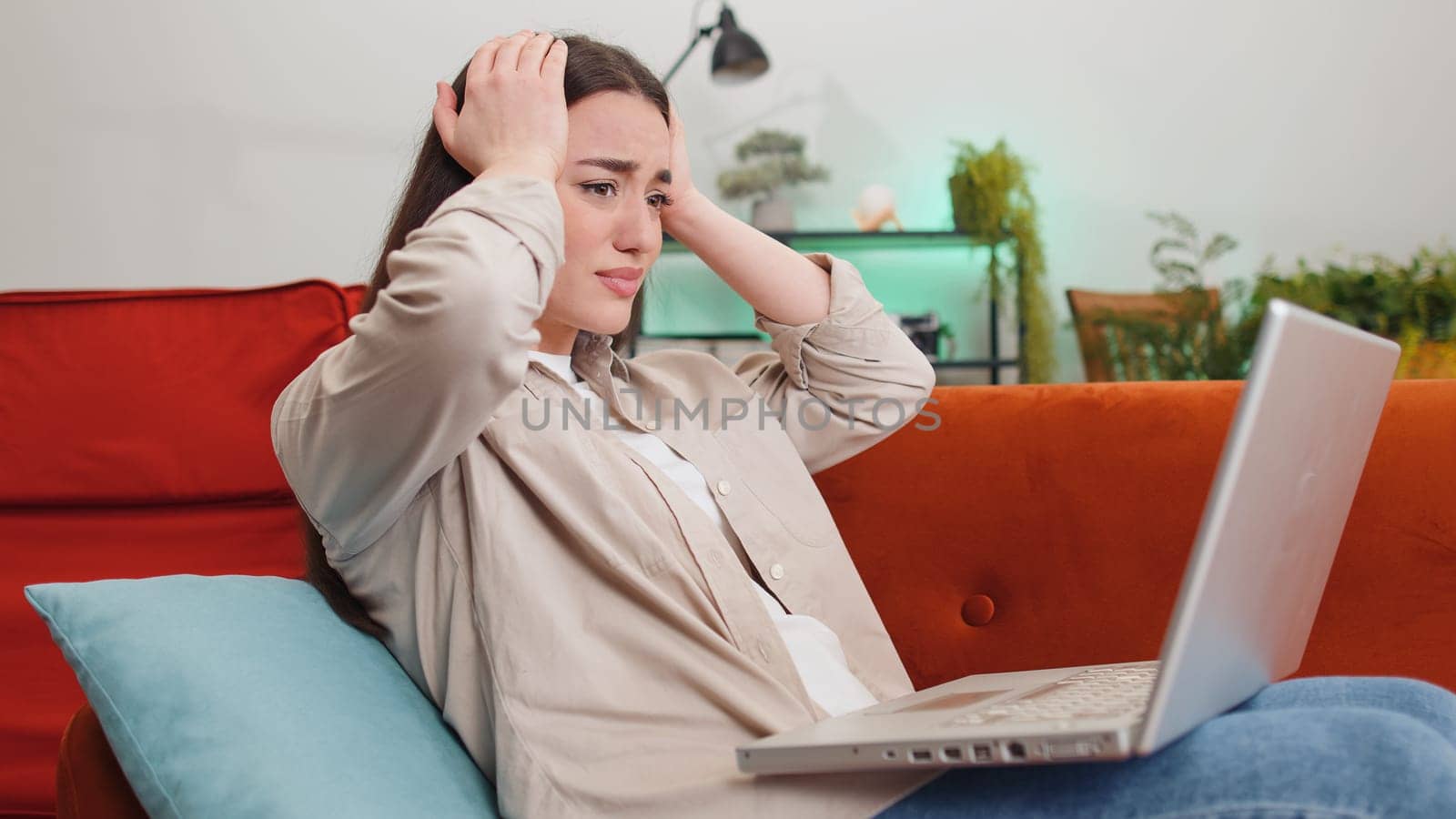 Displeased woman use laptop notebook typing browsing working, loses becoming surprised sudden lottery results bad news fortune loss fail computer virus. Portrait of girl at home in room on couch