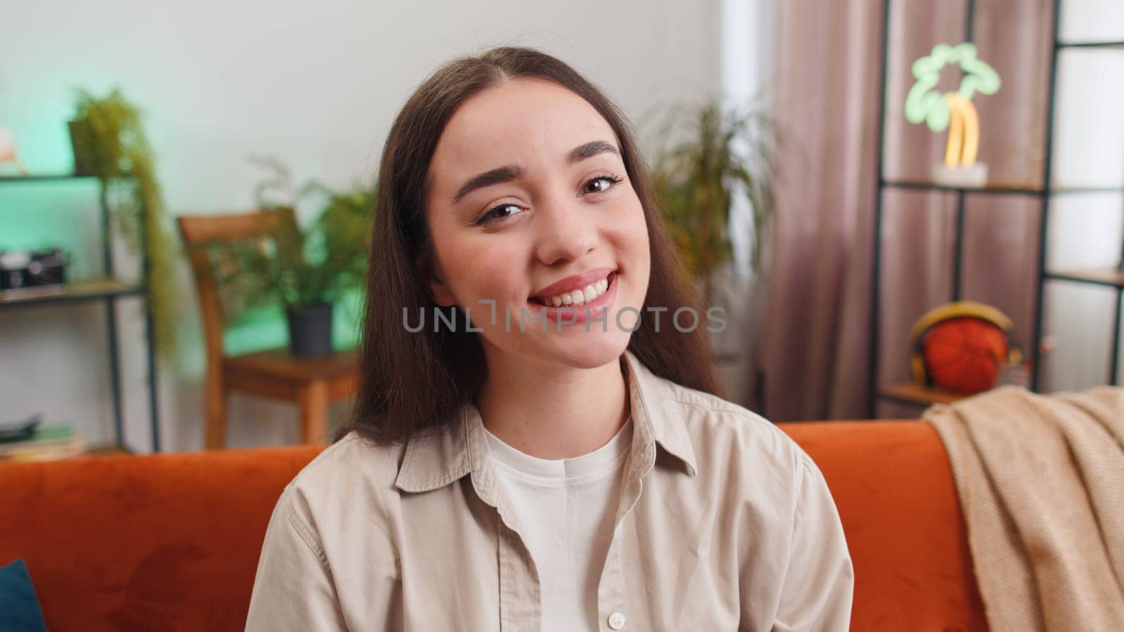 Close-up portrait of happy young woman at home couch smiling friendly, glad expression looking at camera dreaming resting, relaxation feel satisfied concept good news, celebrate win. Girl on room sofa