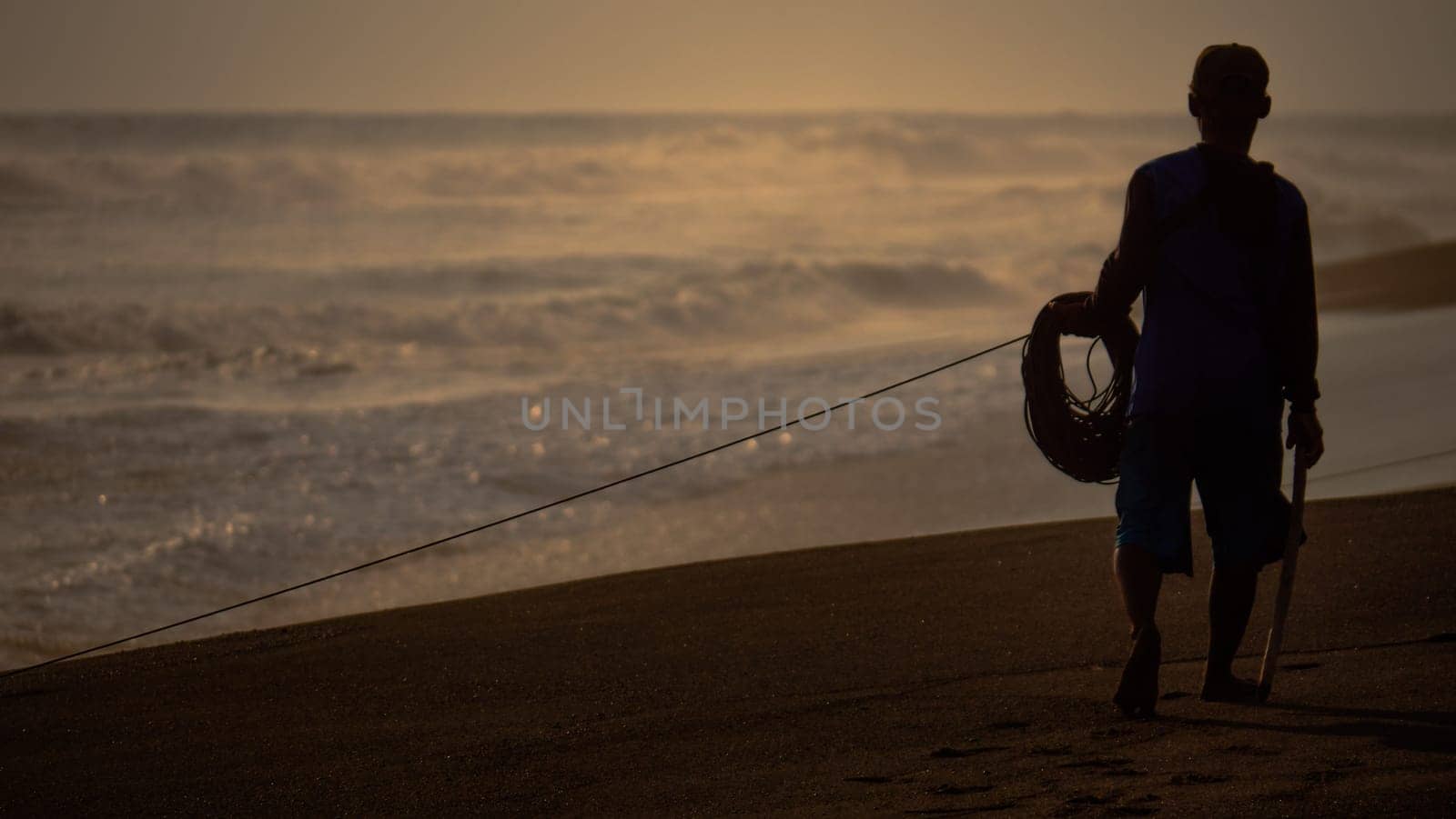 fisherman pulling nets from sea at sunset on sandy beach. Fisherman catching fish in ocean.