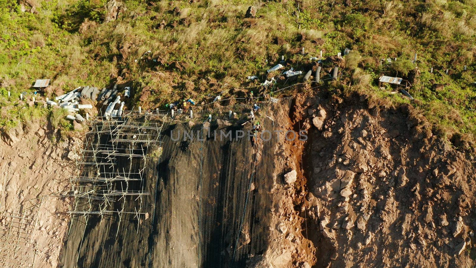 Protection of road from mountain slough, rockfall with metal accumulative restraining net fences. Workers constructing anti-landslide concrete wall prevent protect against rock slides. Rockfall protection. Workers strengthen the slope of the mountain with steel grid preventing rockfall and landslide on the road.