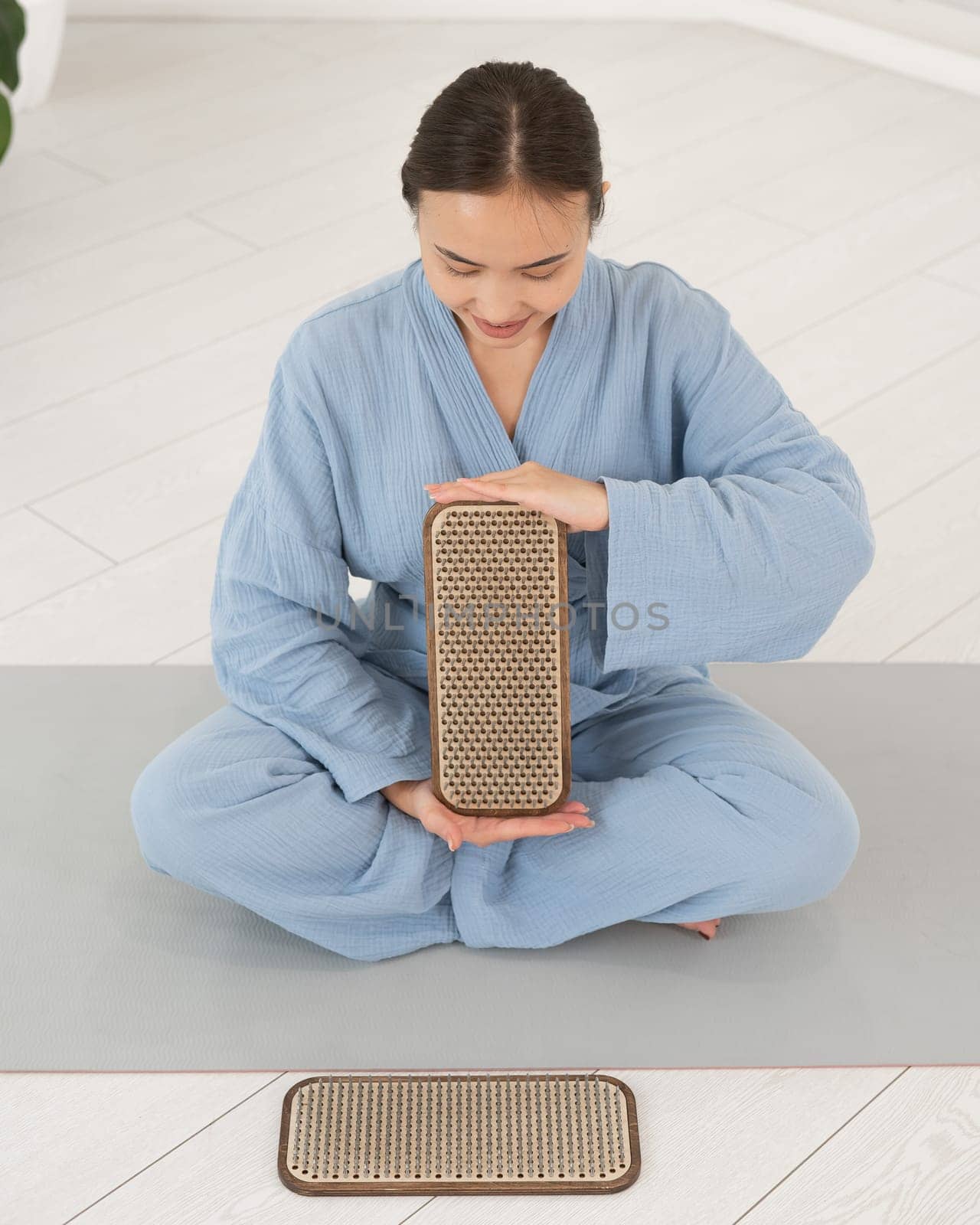 Asian woman sitting in lotus position on yoga mat and holding sadhu boards. by mrwed54