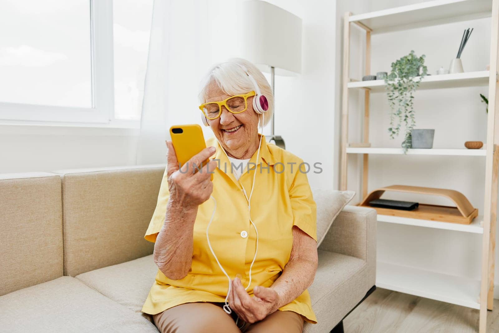 Happy elderly woman looking into phone video call smile, technology for communication, bright modern interior, lifestyle online communication. by SHOTPRIME