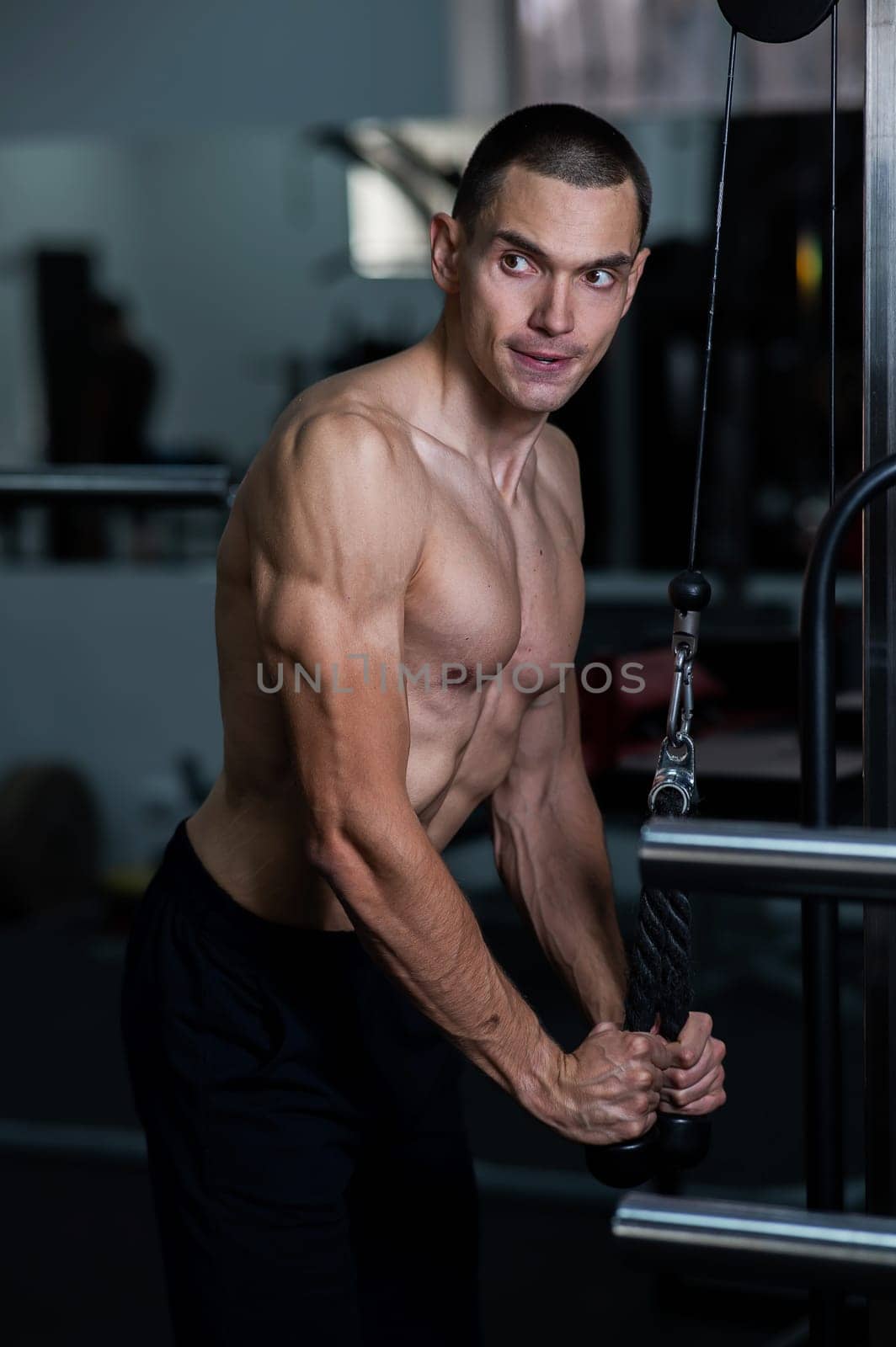 Shirtless man doing triceps pulldown at the gym