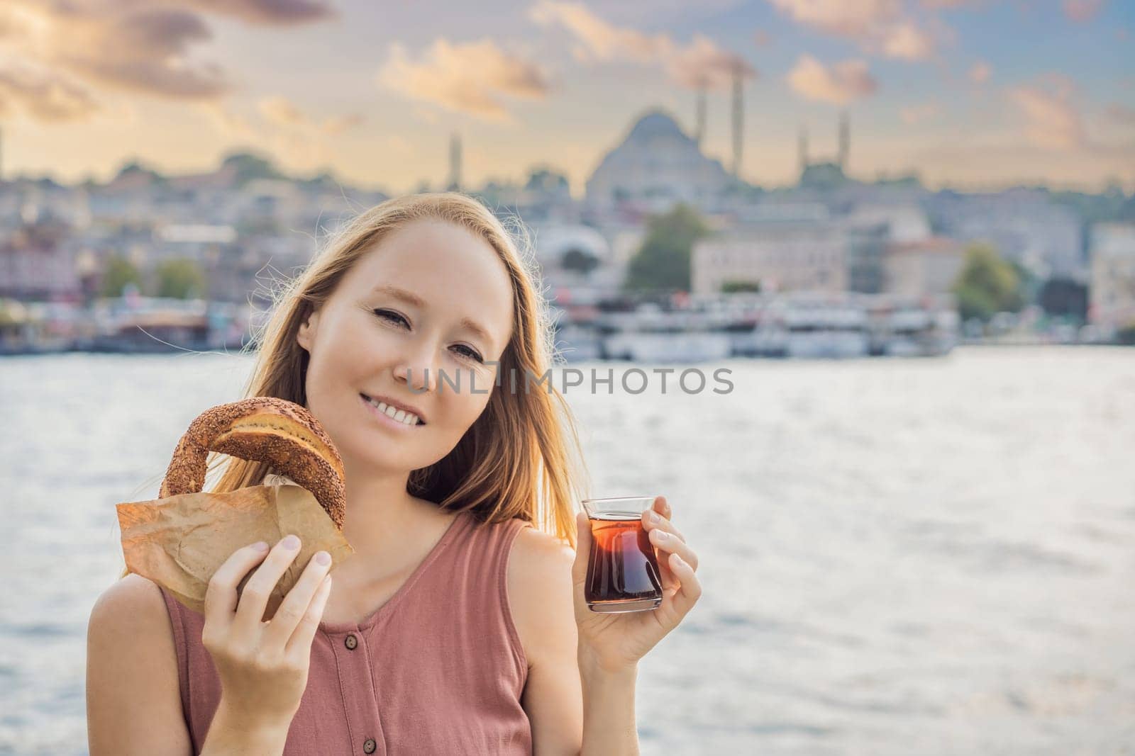Woman in Istanbul having breakfast with Simit and a glass of Turkish tea. Glass of Turkish tea and bagel Simit against golden horn bay in Istanbul, Turkey. Turkiye.