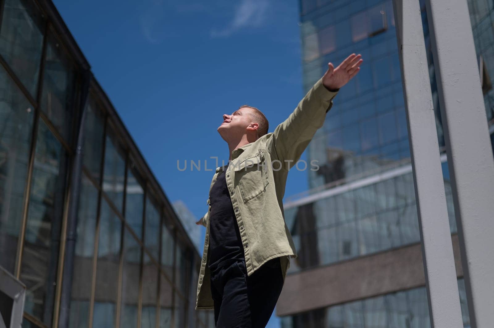 A happy man stands against the backdrop of a skyscraper with his arms spread out to the sides like wings