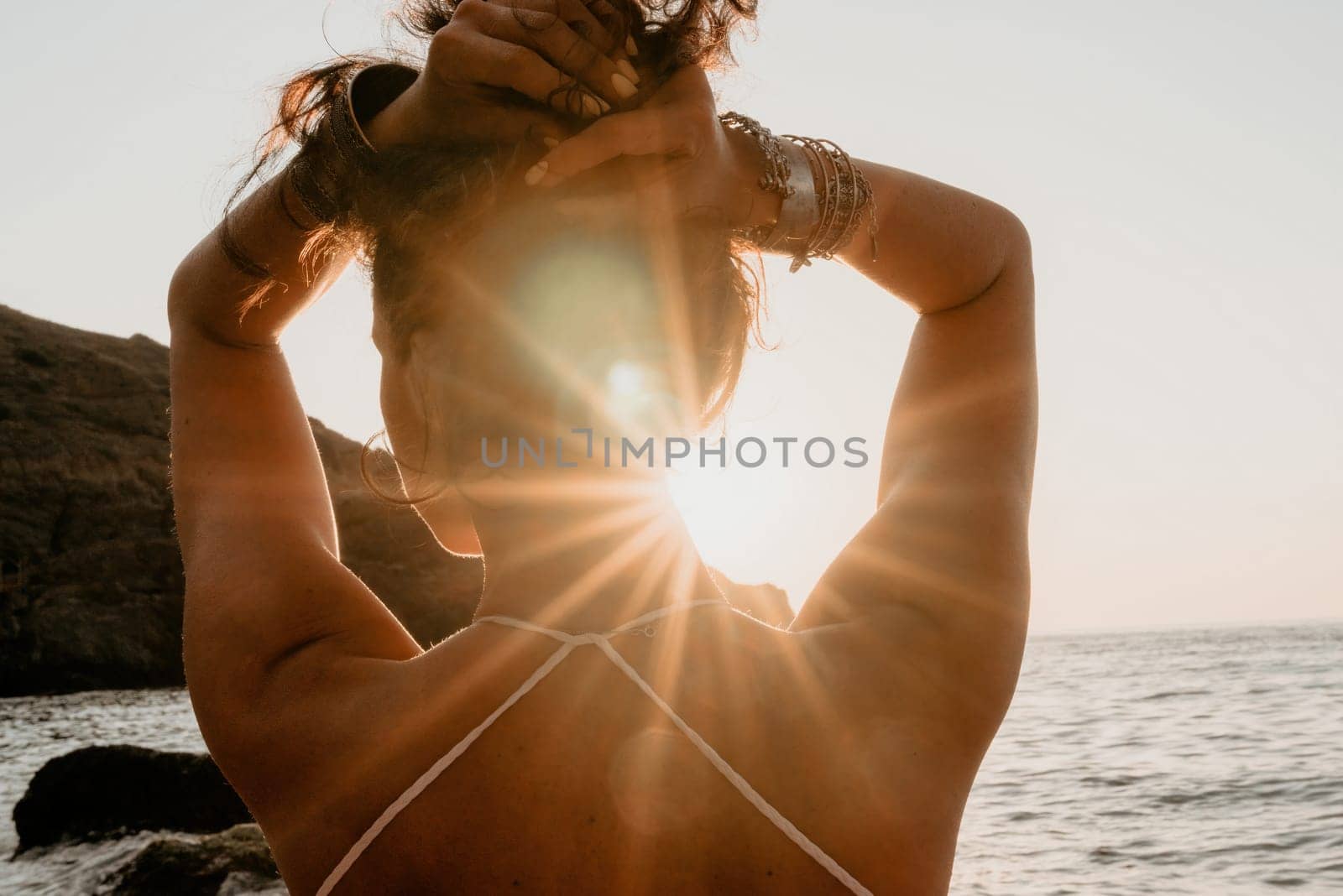 Woman sea yoga. Happy woman in white swimsuit and boho style braclets practicing outdoors on yoga mat by sea on sunset. Women yoga fitness routine. Healthy lifestyle, harmony and meditation by panophotograph