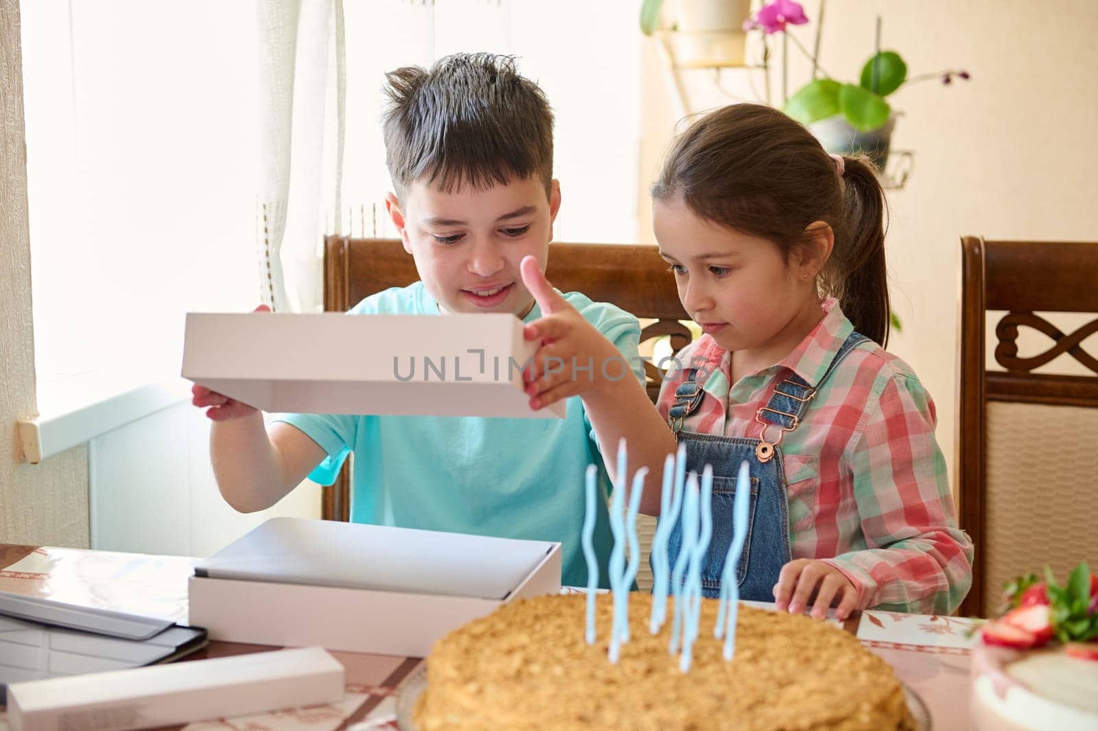 Little girl stands near her brother opening white blank mockup box with happy surprise inside it. Happy birthday concept by artgf