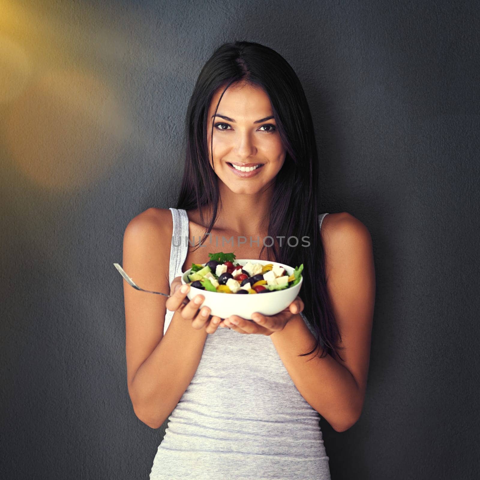 Its a bowl full of goodness. Portrait of a healthy young woman eating a salad against a gray background. by YuriArcurs