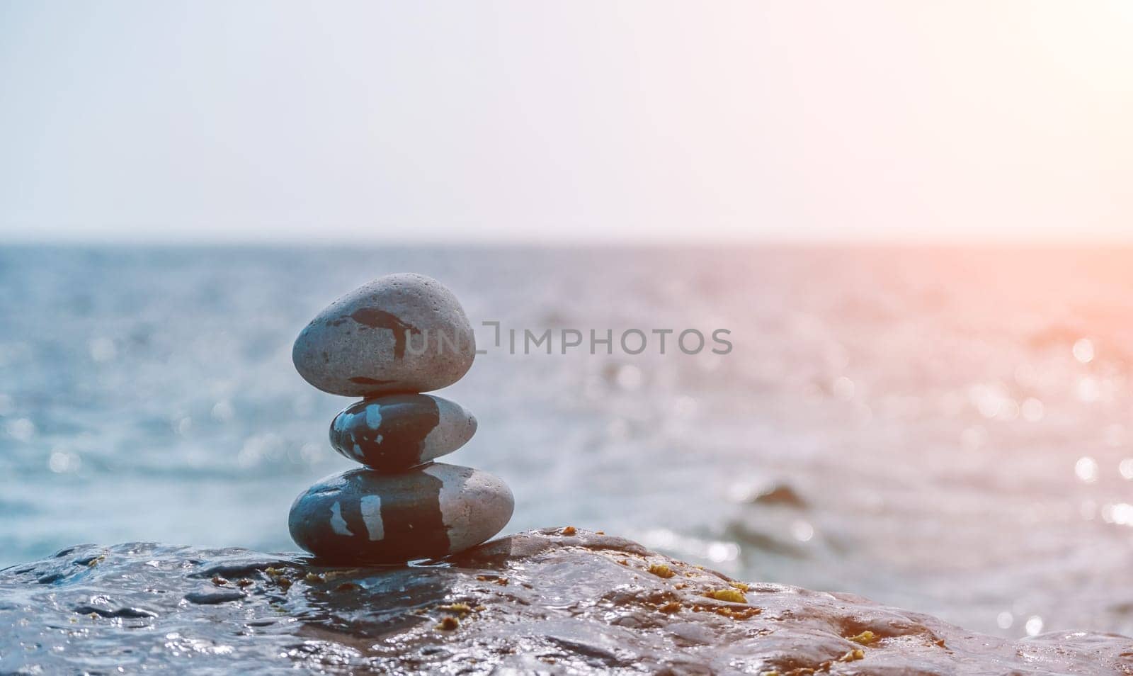 Pyramid stones on the seashore with warm sunset on the sea background. Happy holidays. Pebble beach, calm sea, travel destination. Concept of happy vacation on the sea, meditation, spa, calmness.