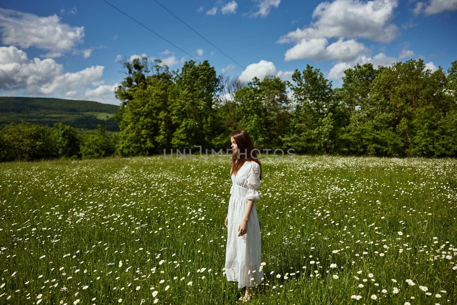 a woman in a long light dress stands in a chamomile field on a sunny day by Vichizh