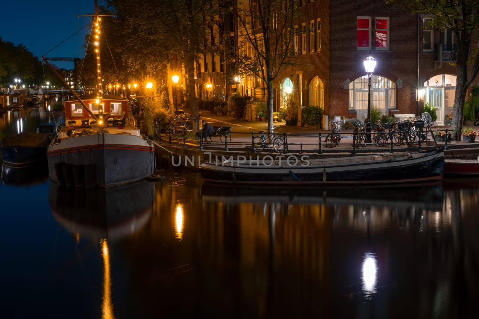 Netherlands. Summer night in Amsterdam. Canal quay with residential barges and bicycles