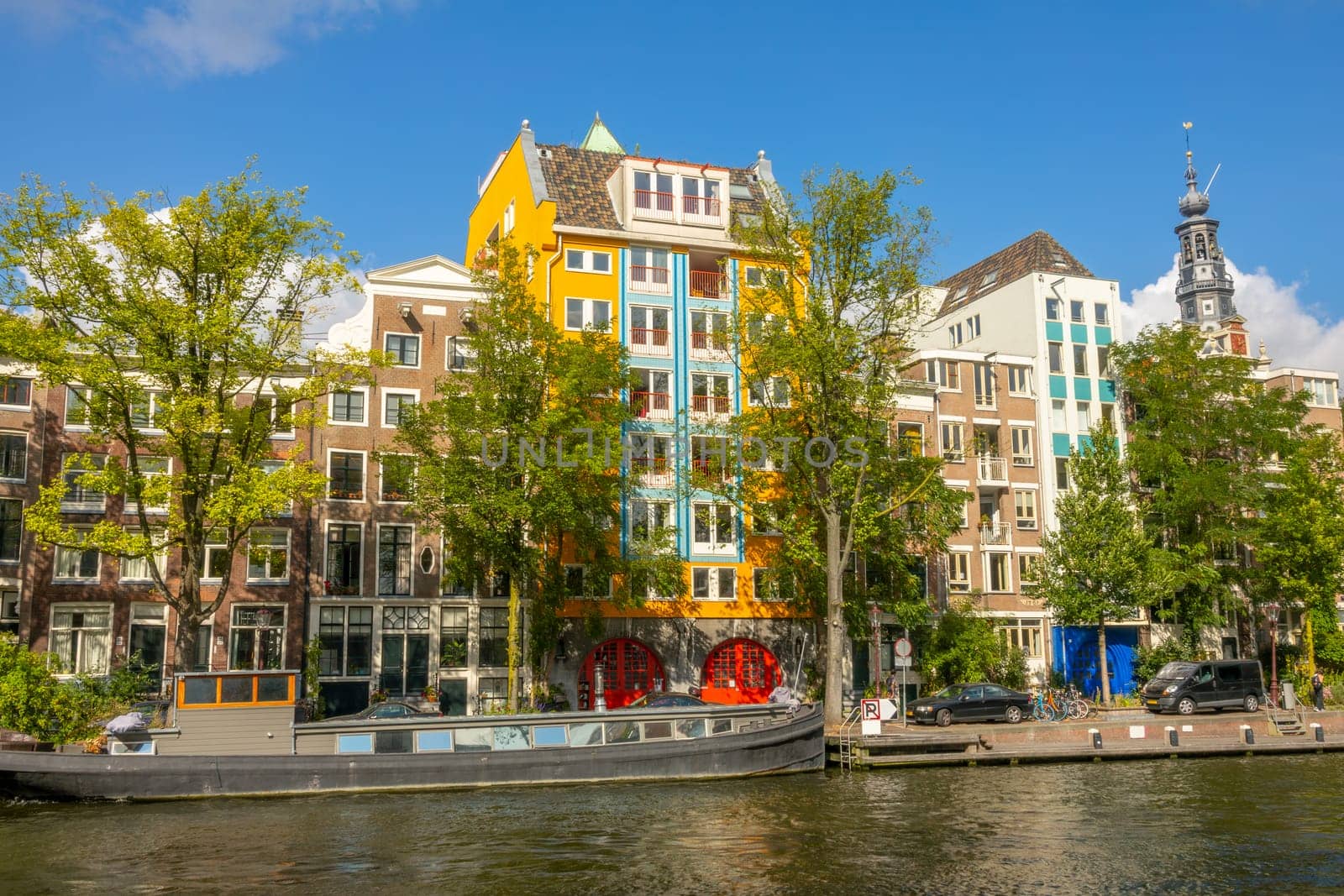 Netherlands. Sunny summer day on the Amsterdam Canal. Facades of typical Dutch buildings and residential barge at the pier