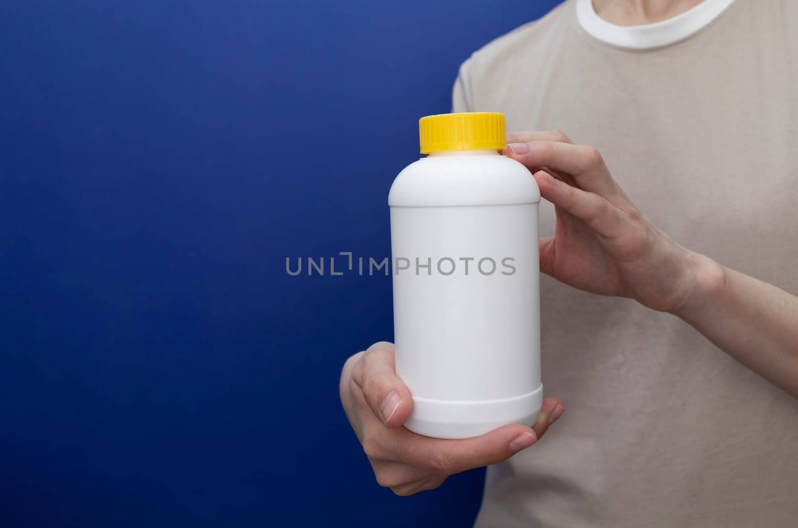 Female Holds White Plastic Bottle With Pipe Cleaner Granules On Blue Background Removal Of Blockage In Sink, Shower With Special Chemicals. Cleaning Clog In Kitchen, Bathroom. Copy space, Horizontal