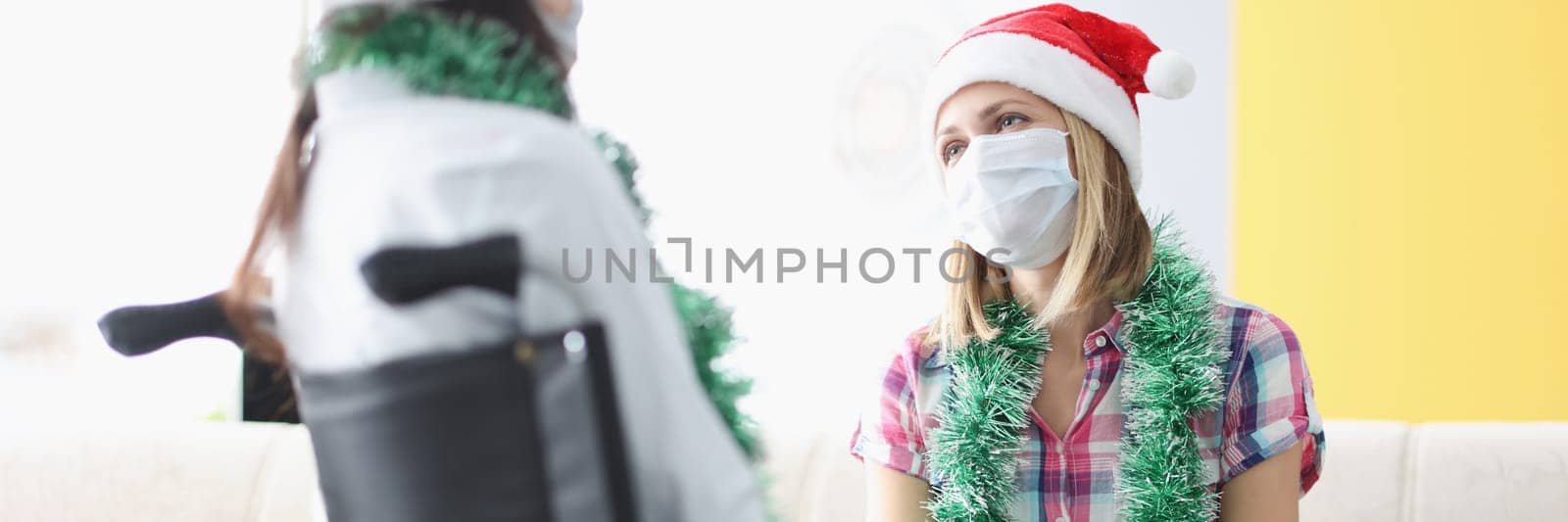 Portrait of female visiting sister in clinic, relative sitting in wheelchair, face mask for protection. Healthcare, medicine, disabled people, family, pandemic, new year concept
