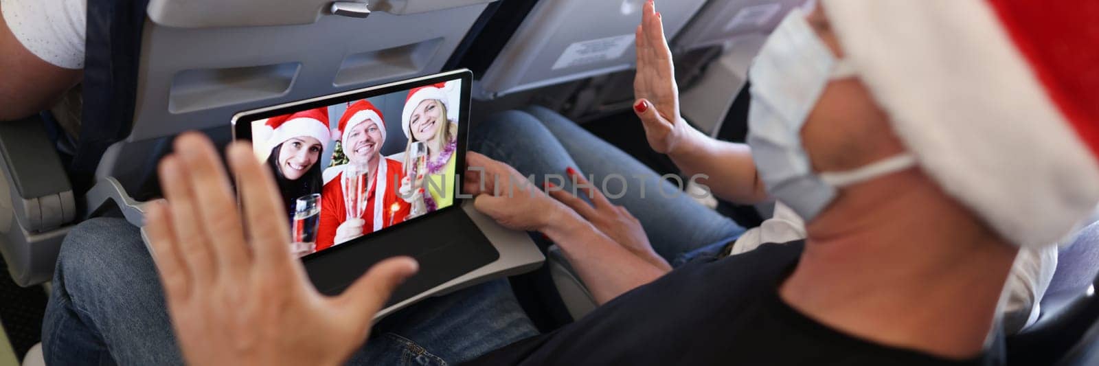 Close-up of man in face mask and santa claus hat talk to family on new year, say hello and congratulate on distance, celebrate holiday in air. Christmas, flight, festive mood concept