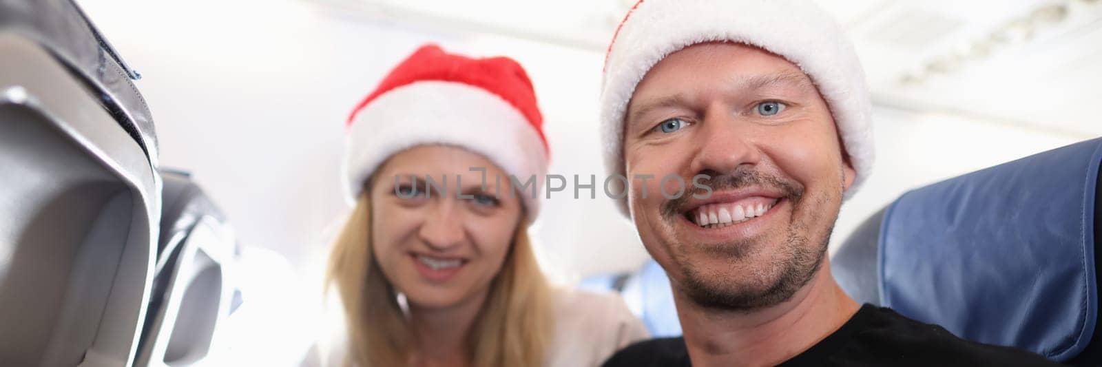 Man and woman in red santa hats flying in airplane by kuprevich