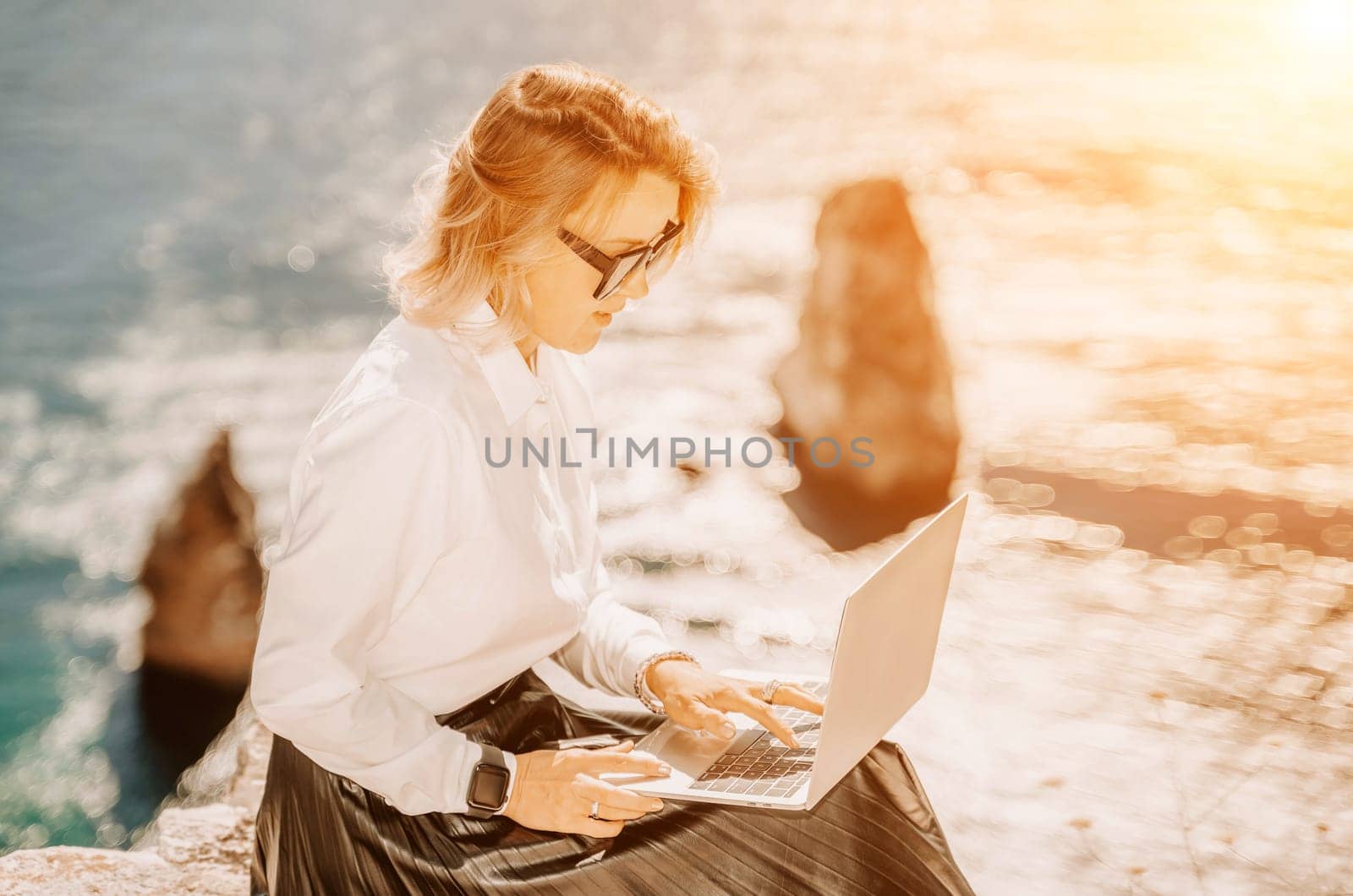 Business woman on nature in white shirt and black skirt. She works with an iPad in the open air with a beautiful view of the sea. The concept of remote work