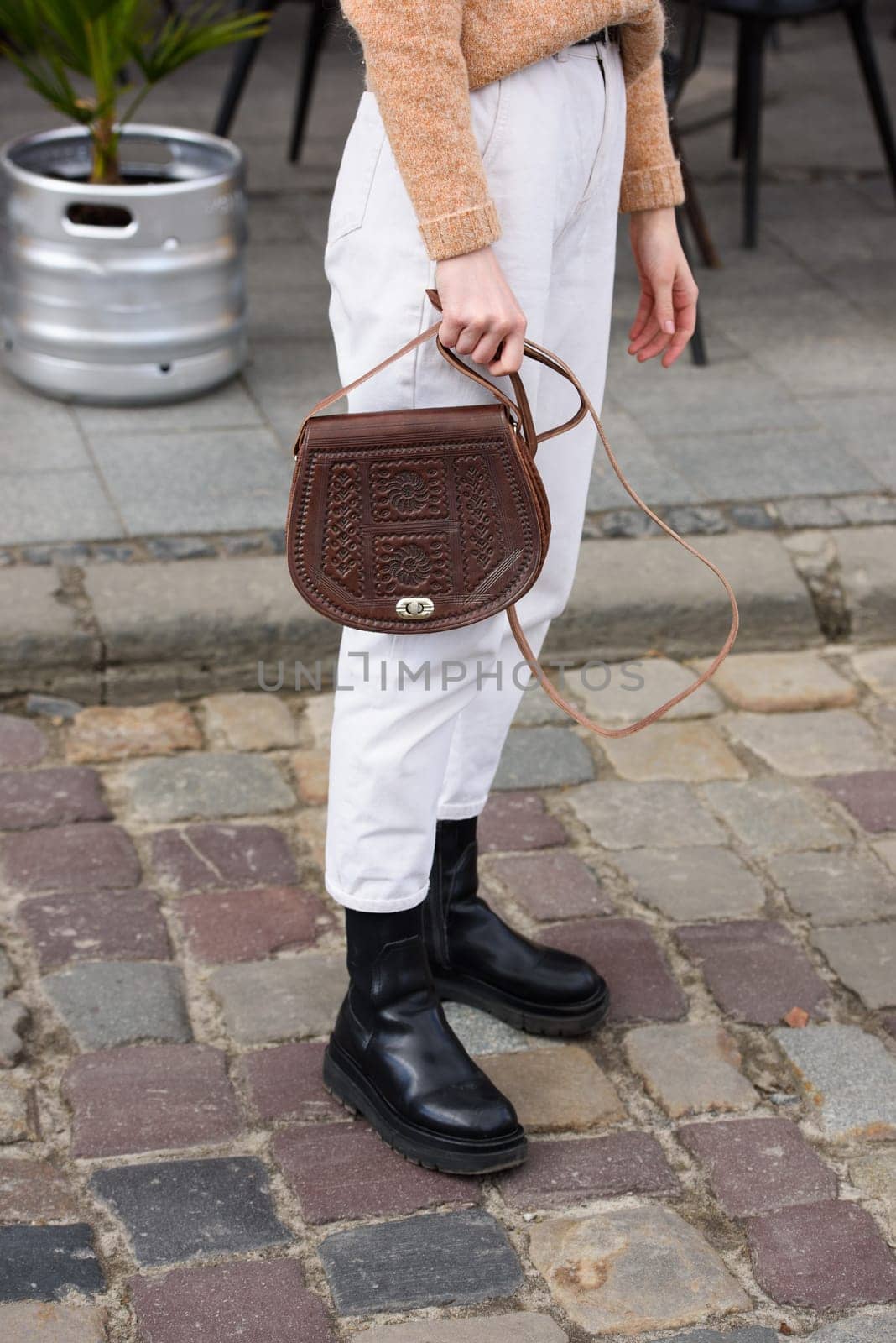 woman in white pants and a beige sweater poses outside with a small leather handbag by Ashtray25