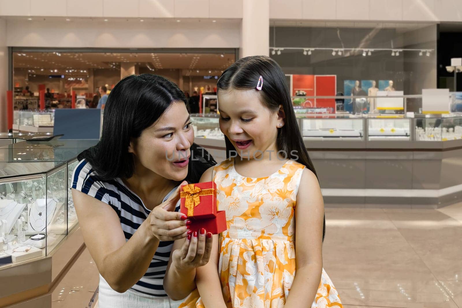 Mother opens a red gift box for her little girl. Childs birthday concept. Woman and her daughter in the mall.