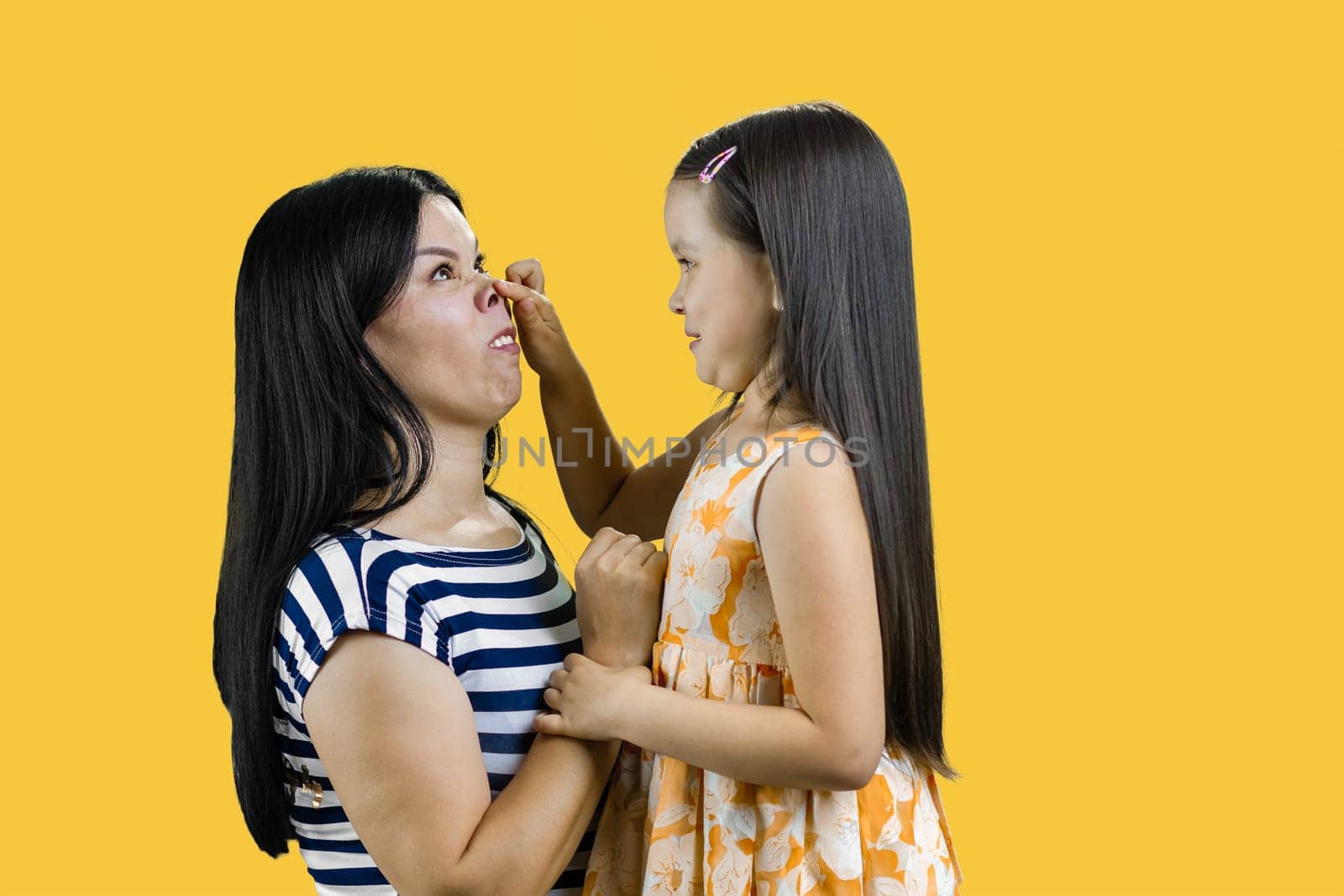 Little girl is making a piggy nose to her mother. Isolated on yellow.