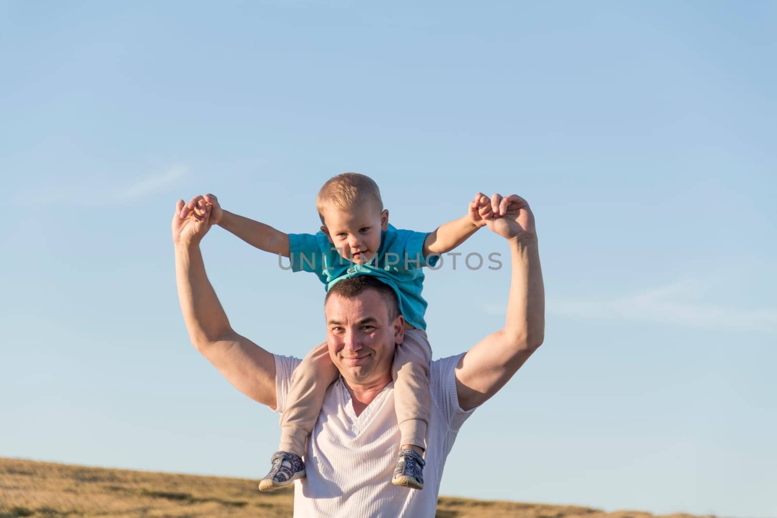 Dad and his little son are having fun walking in a field with ripe wheat. The child is sitting on the shoulders of the father. Grain for making bread. the concept of economic crisis and hunger