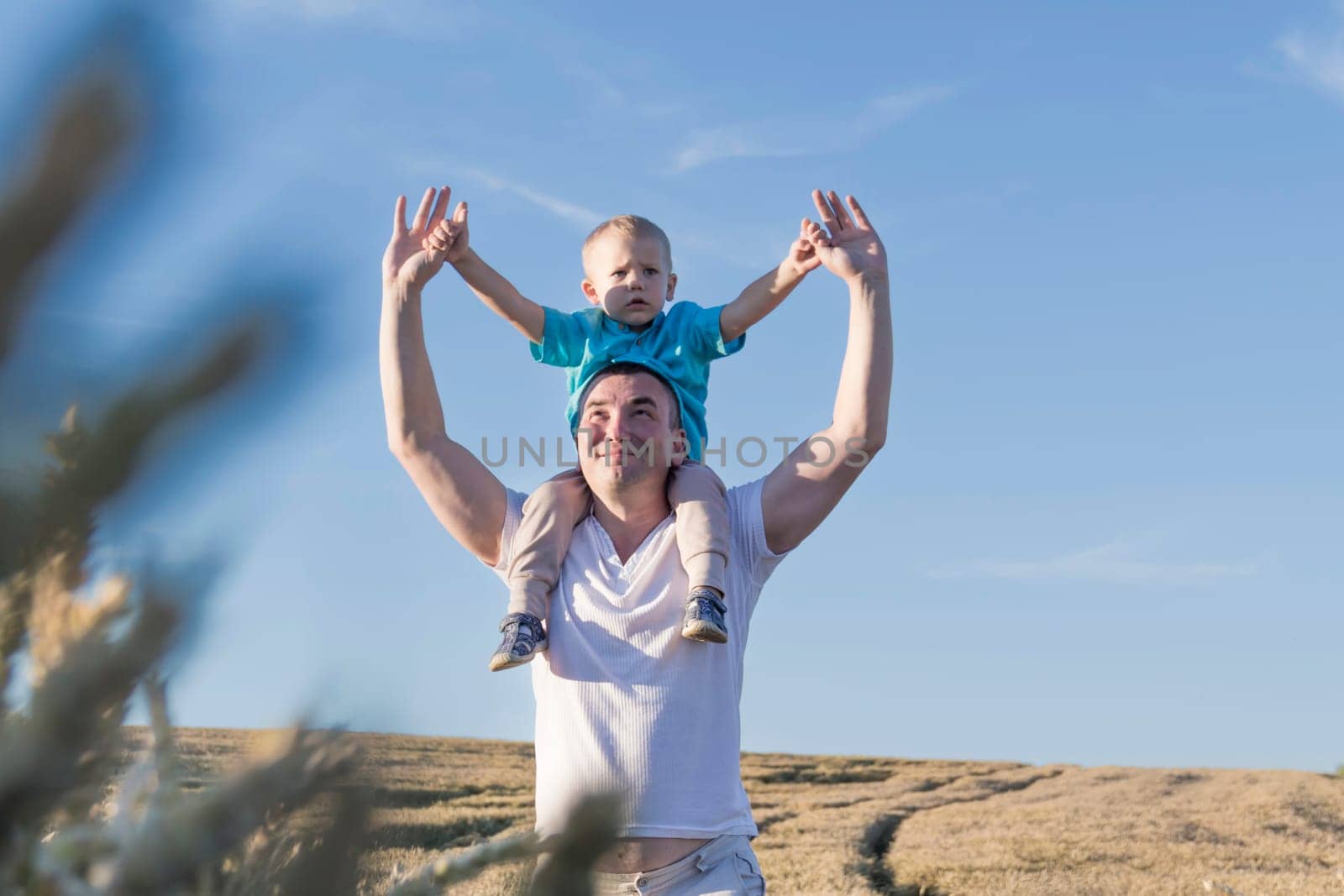 Dad and his little son are having fun walking in a field with ripe wheat. The child is sitting on the shoulders of the father. Grain for making bread. the concept of economic crisis and hunger