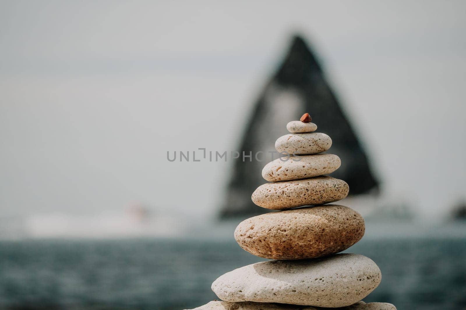 Pyramid stones on the seashore with warm sunset on the sea background. Happy holidays. Pebble beach, calm sea, travel destination. Concept of happy vacation on the sea, meditation, spa, calmness.