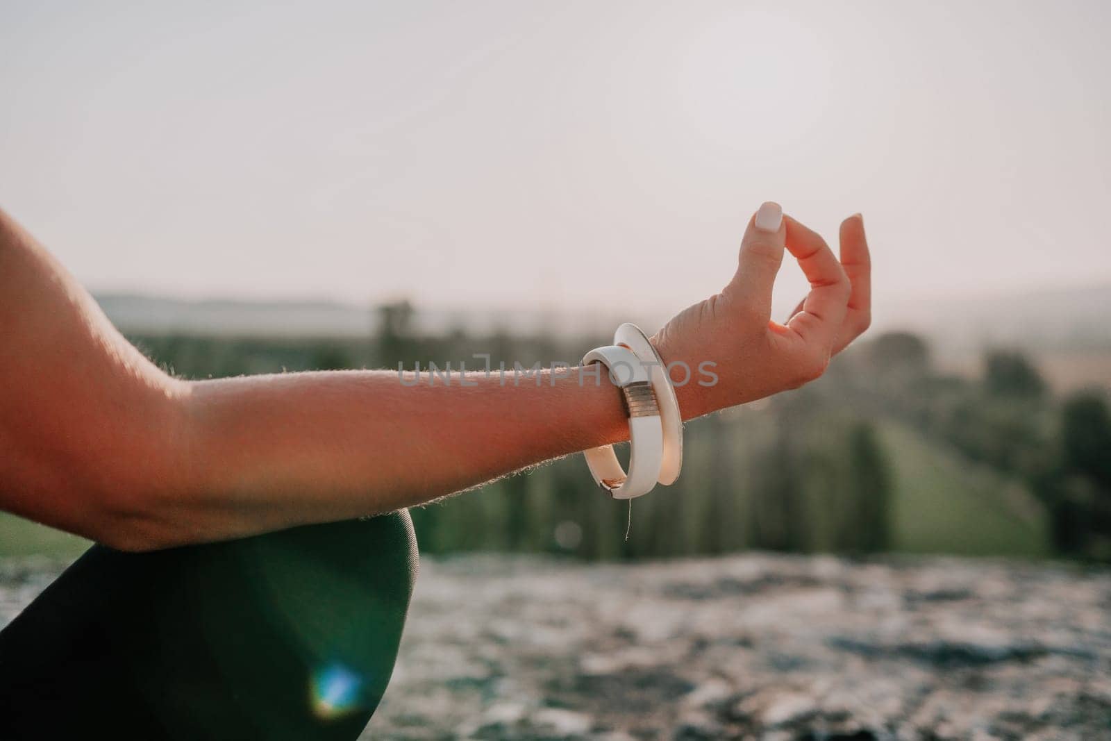 Well looking middle aged woman with long hair, fitness instructor in leggings and tops doing stretching and pilates on the rock near forest. Female fitness yoga routine concept. Healthy lifestyle.