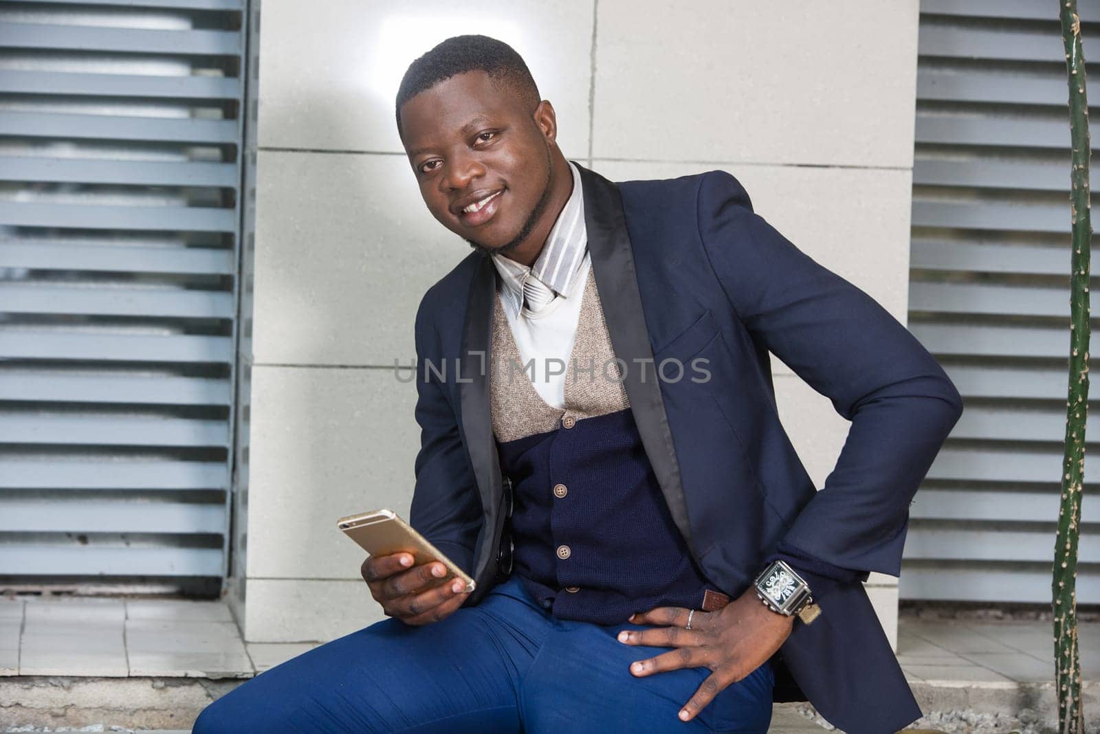 young man sitting in suit with mobile phone in hand watching the camera smiling.