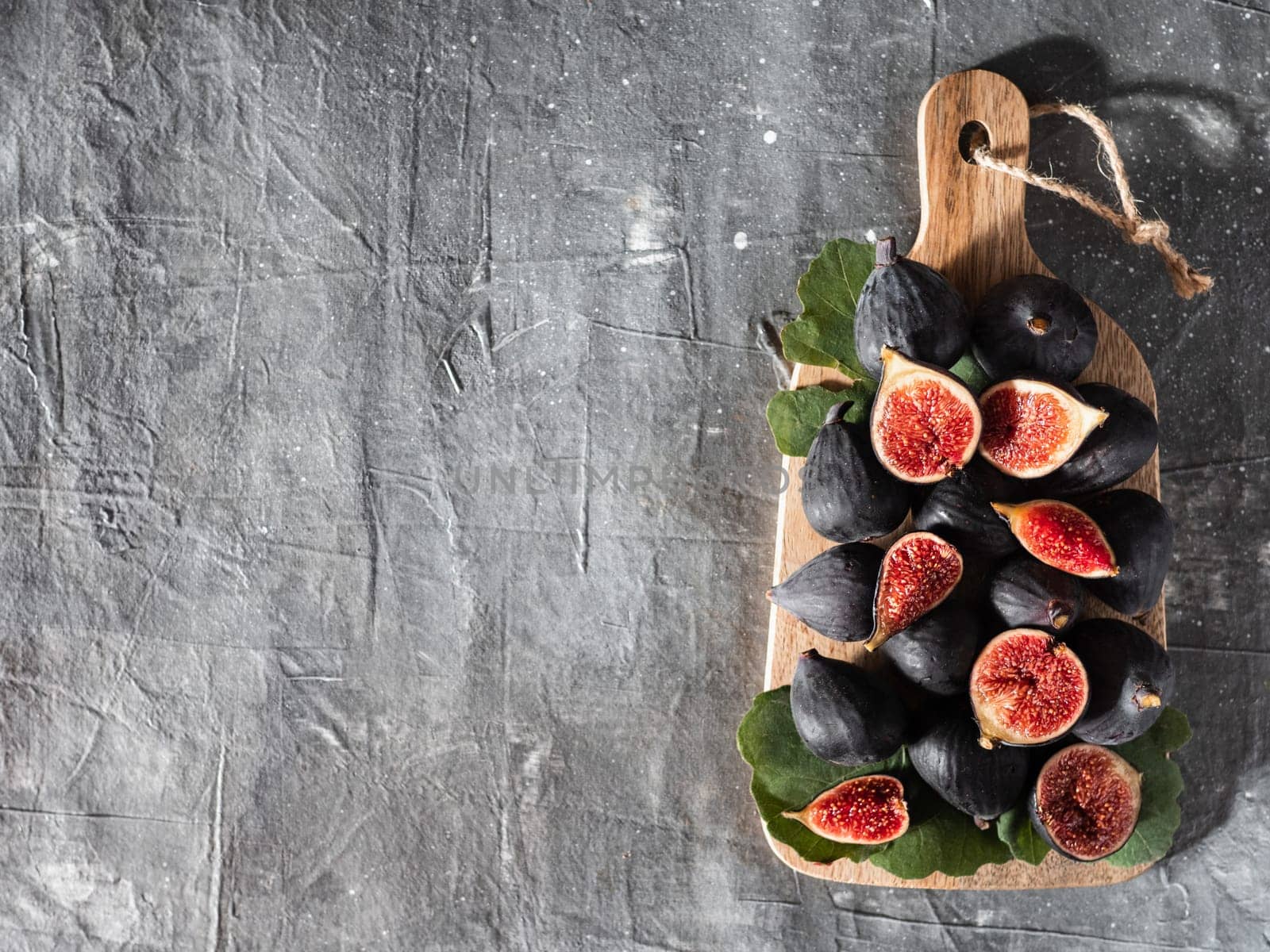 Figs with copy space. Top view of whole and half fresh purple figs on wooden cutting board over gray background.