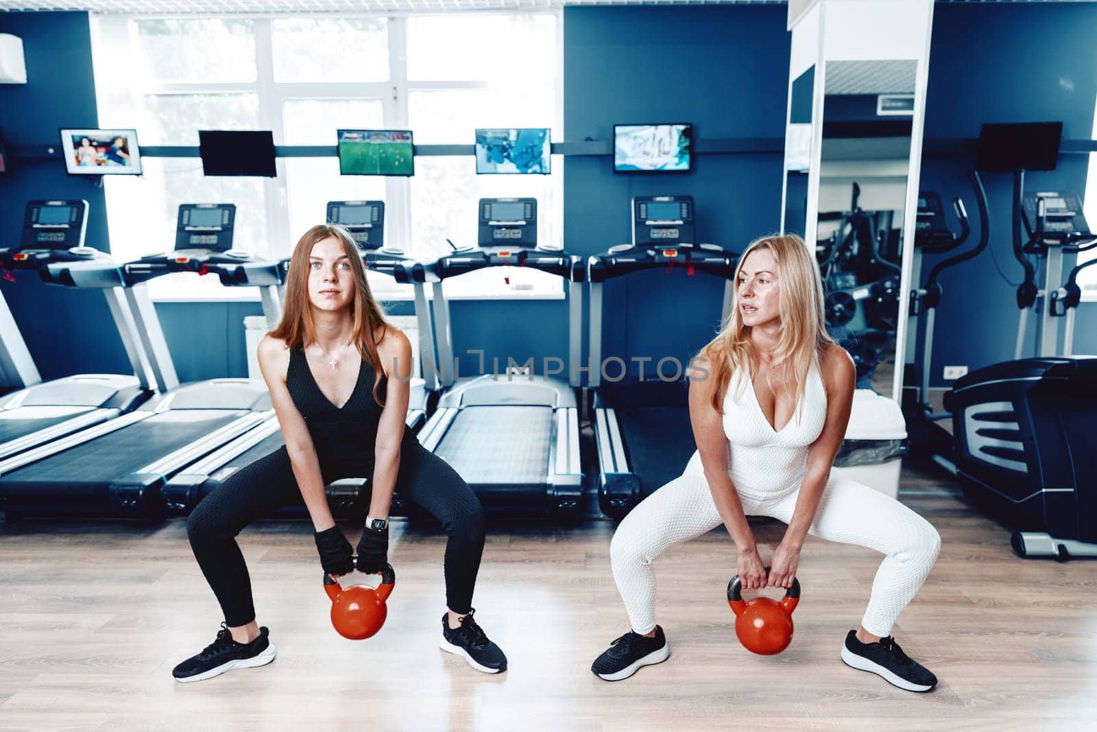 Mother and daughter in sportswear exercising with dumbbells in the gym by Fabrikasimf