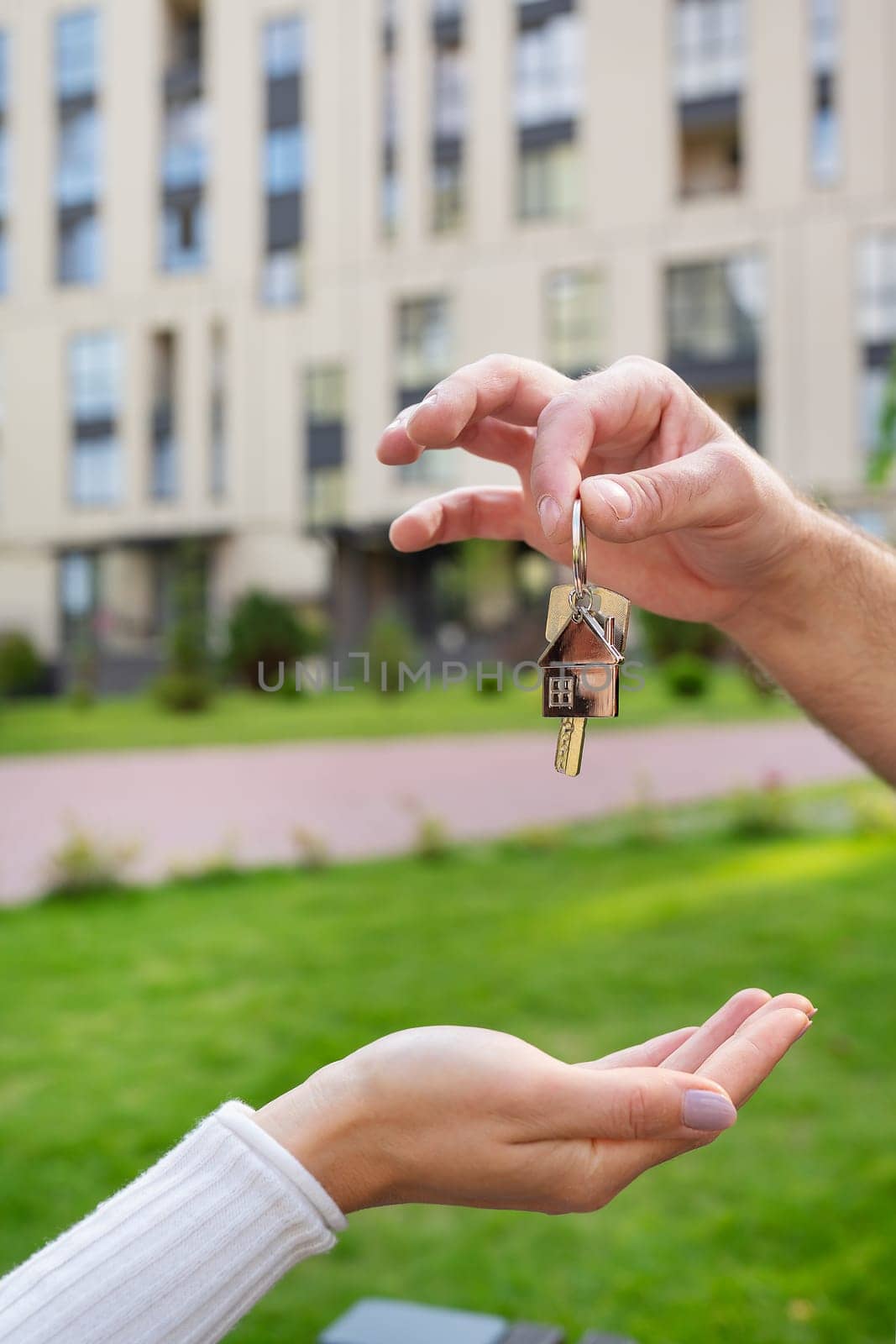 Keys with a keychain in the form of a metal house from a new house or apartment in the hands of a young family. Happiness from buying a house. Handing over the keys from the realtor. by sfinks